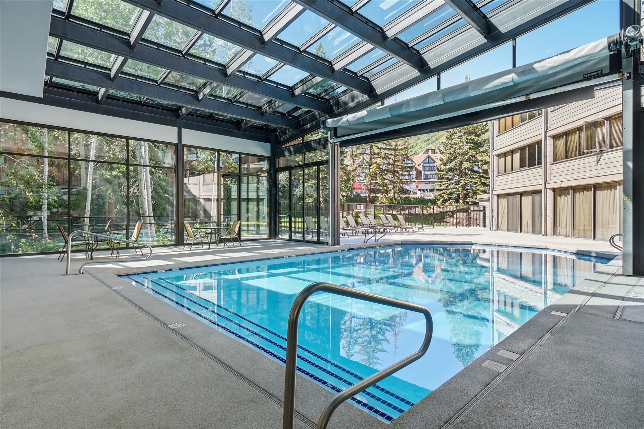 Indoor pool featuring a clear glass roof, full-height exterior glass walls, and a large opening to an outdoor patio with additional seating
