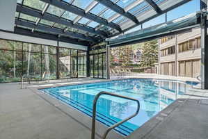 Indoor pool featuring a clear glass roof, full-height exterior glass walls, and a large opening to an outdoor patio with additional seating