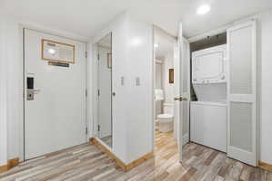 Wood-finish flooring throughout, featuring a stacked washer and dryer in a louvered bi-fold door closet, and a partial view of a bathroom with a white toilet