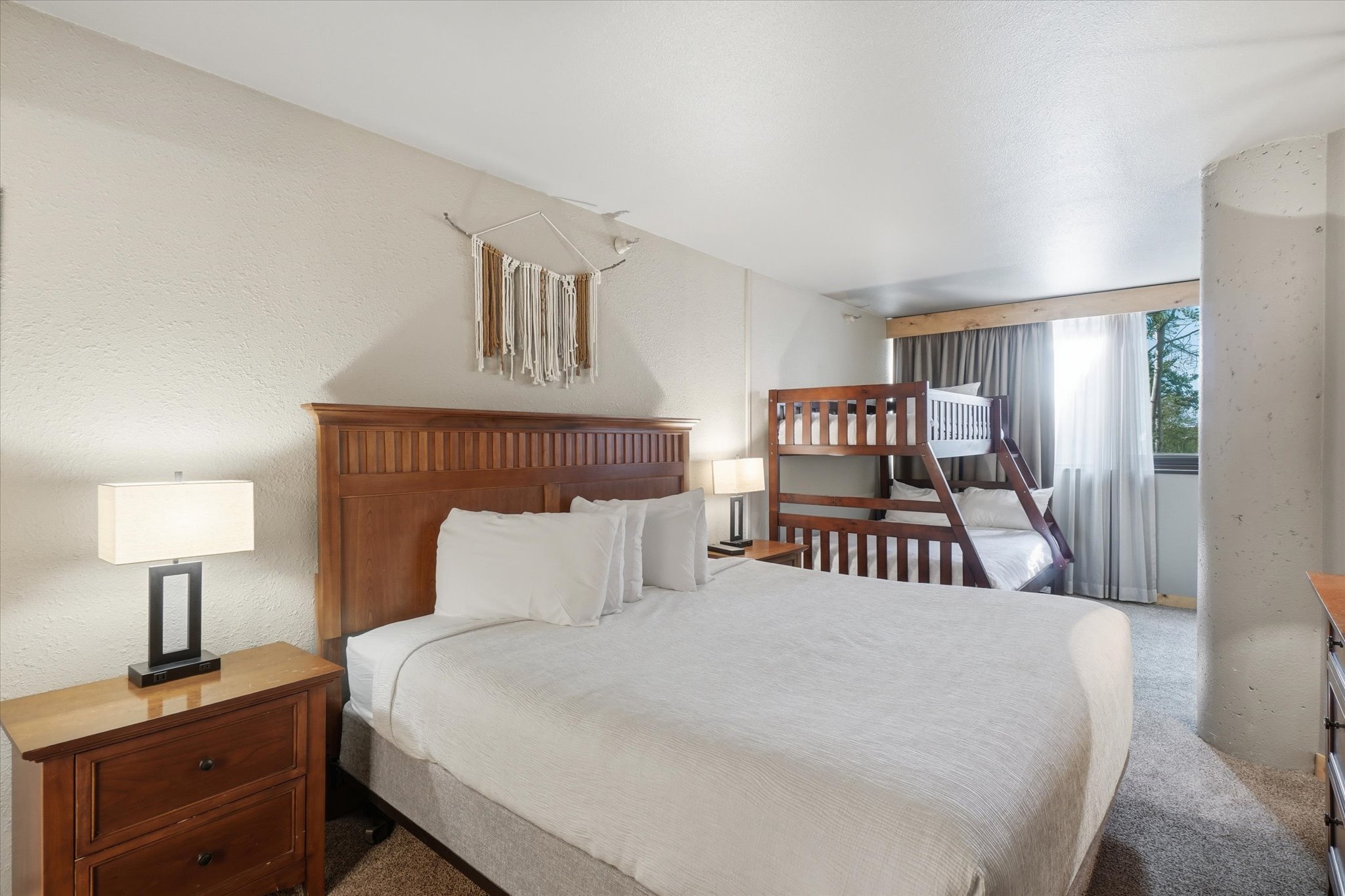 Carpeted room featuring a wooden headboard, two-drawer nightstand, and a bunk bed with a ladder
