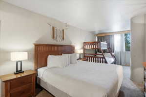 Carpeted room featuring a wooden headboard, two-drawer nightstand, and a bunk bed with a ladder
