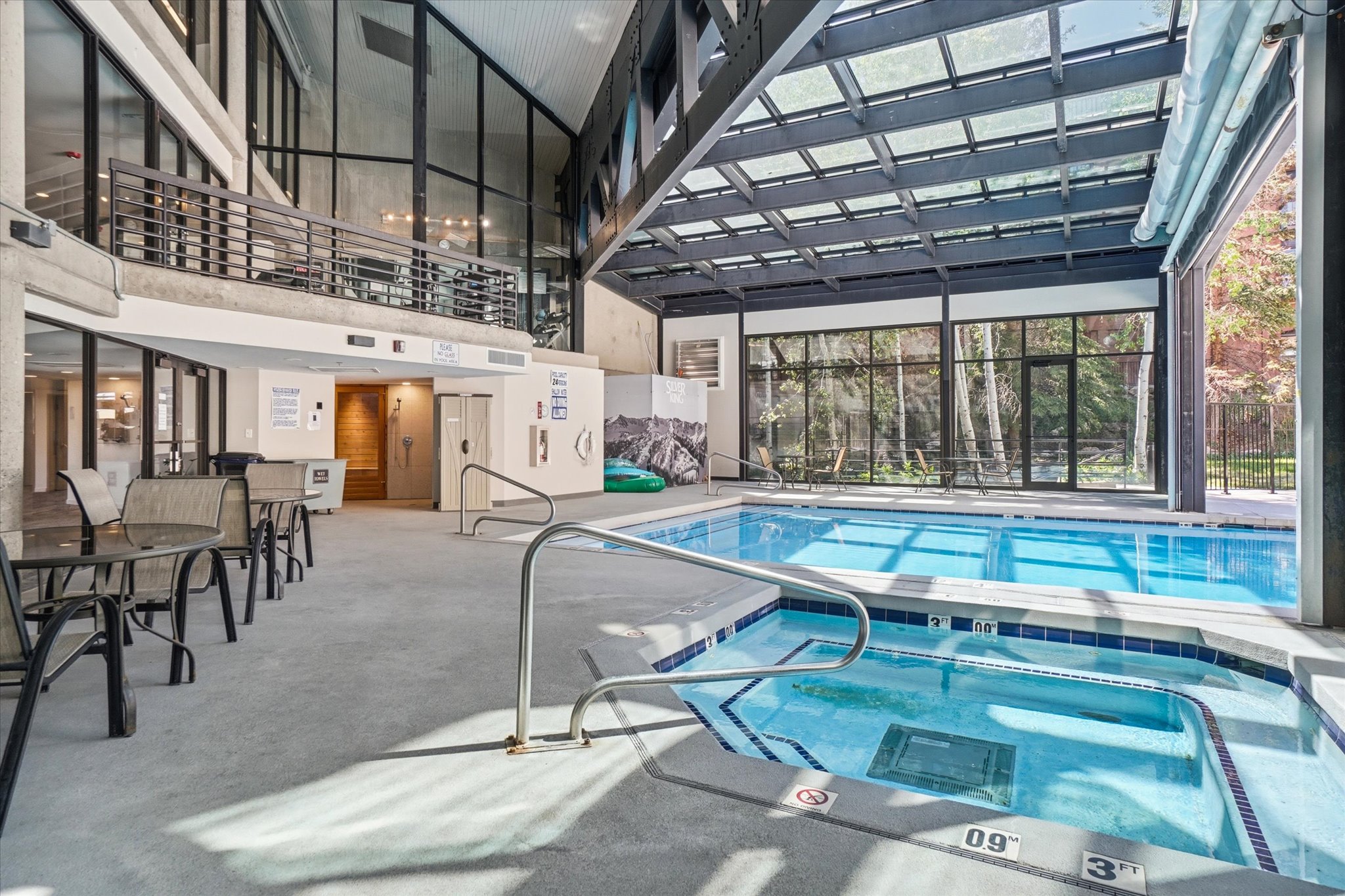Indoor pool and hot tub area featuring a large skylight roof, extensive window walls, and access to an upper-level balcony