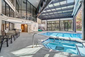 Indoor pool and hot tub area featuring a large skylight roof, extensive window walls, and access to an upper-level balcony