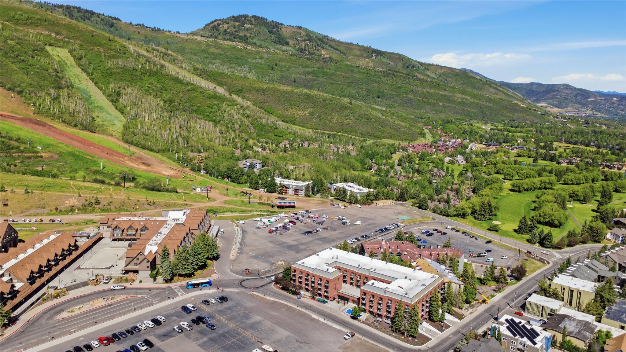 Expansive aerial perspective showcasing a mountainous landscape with ski slopes, a golf course, and multiple buildings