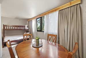 Open concept room featuring a wood-finish dining table and chairs, bunk beds, and large windows with privacy drapes