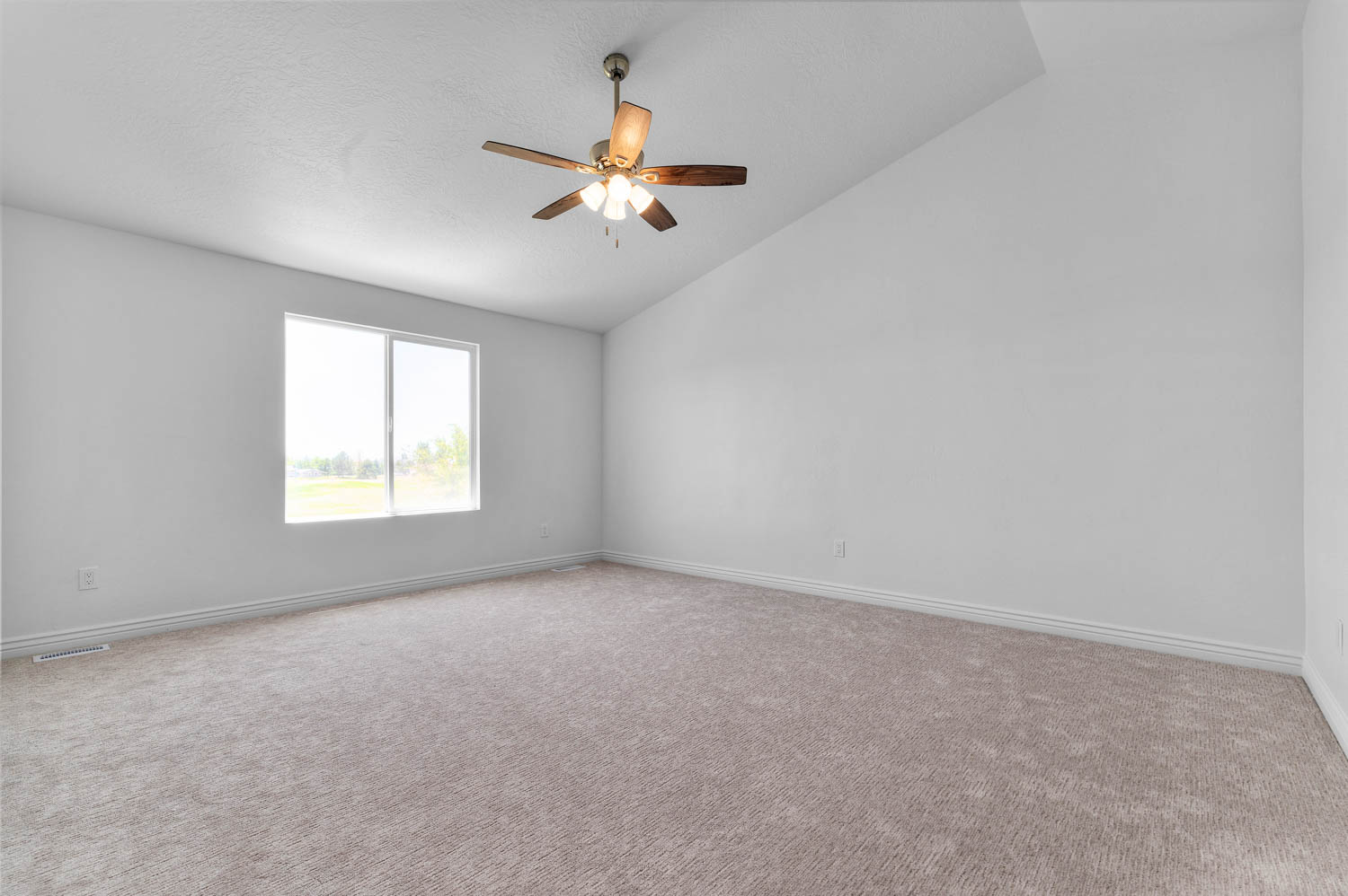 Spacious room featuring vaulted ceilings, light gray carpeting, a large window, a ceiling fan with integrated lighting, and white baseboards