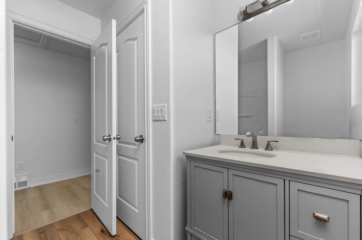 Bathroom vanity featuring a light gray cabinet with brushed nickel hardware, a white countertop with an integrated sink, and a large mirror with a three-bulb light fixture