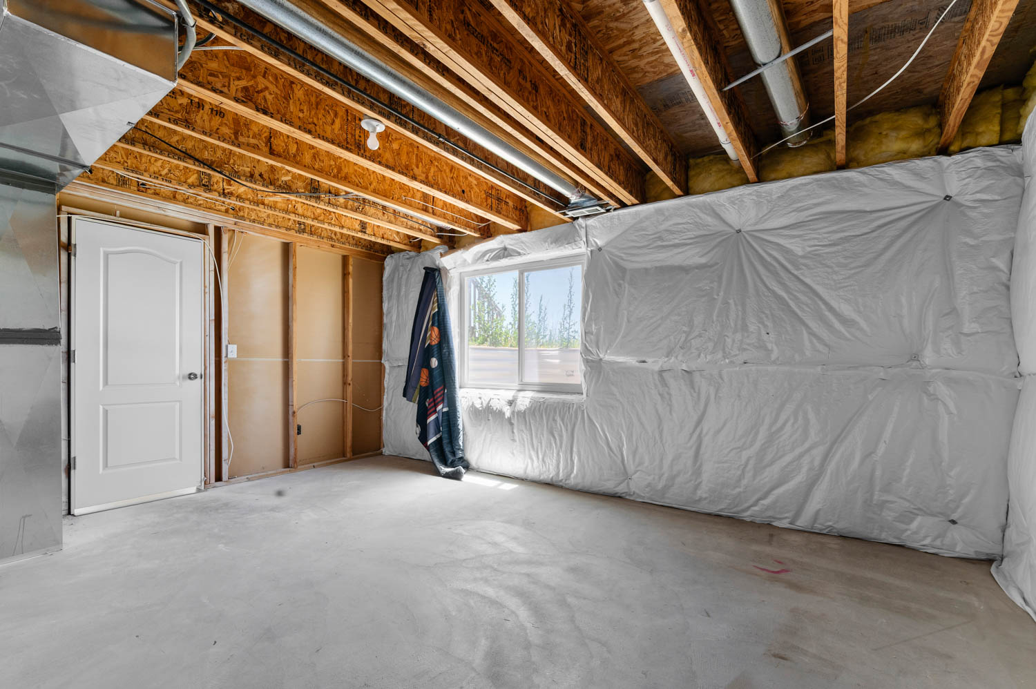 Unfinished basement space featuring exposed wood joists and subfloor, a single window, and a white interior door