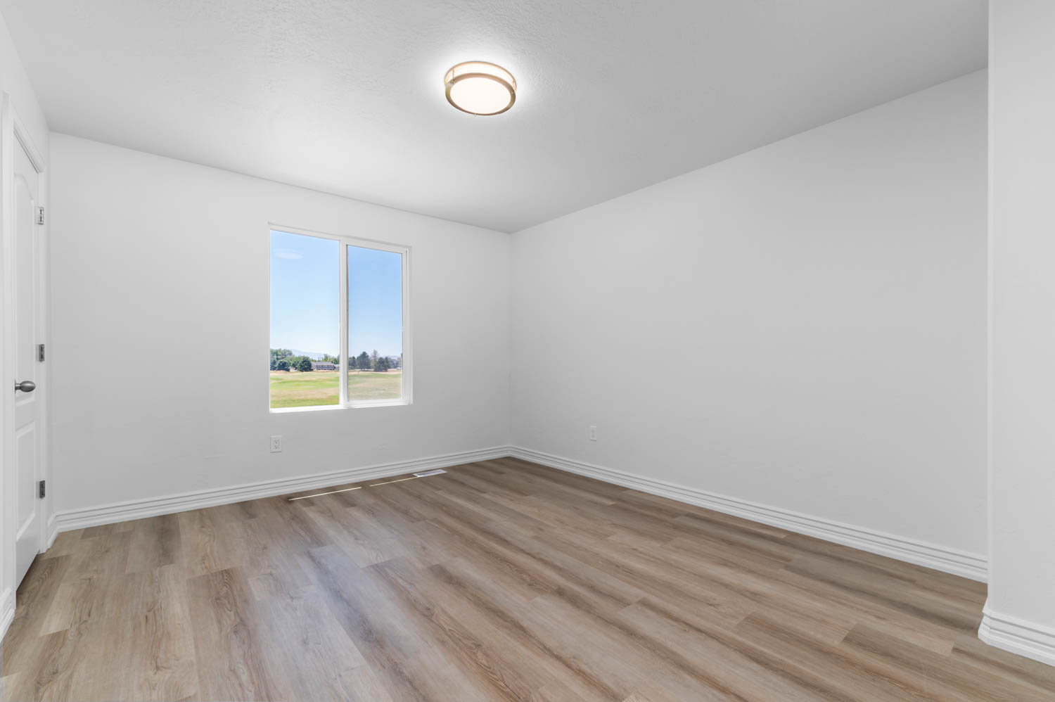 Bright room featuring wood-finish flooring, a double-pane window, white baseboards, and a contemporary flush-mount ceiling light