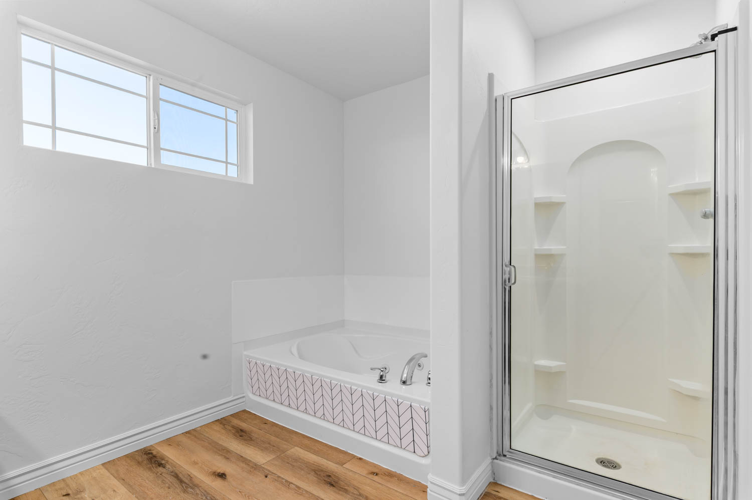Full bathroom featuring a walk-in shower with built-in shelving, a soaking tub with decorative tile surround, and wood-finish flooring