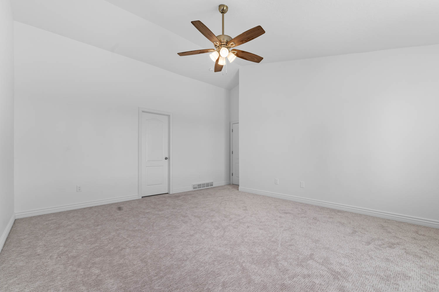 Spacious room featuring vaulted ceilings, a ceiling fan with light fixture, light gray carpeting, white baseboards, and a white two-panel interior door