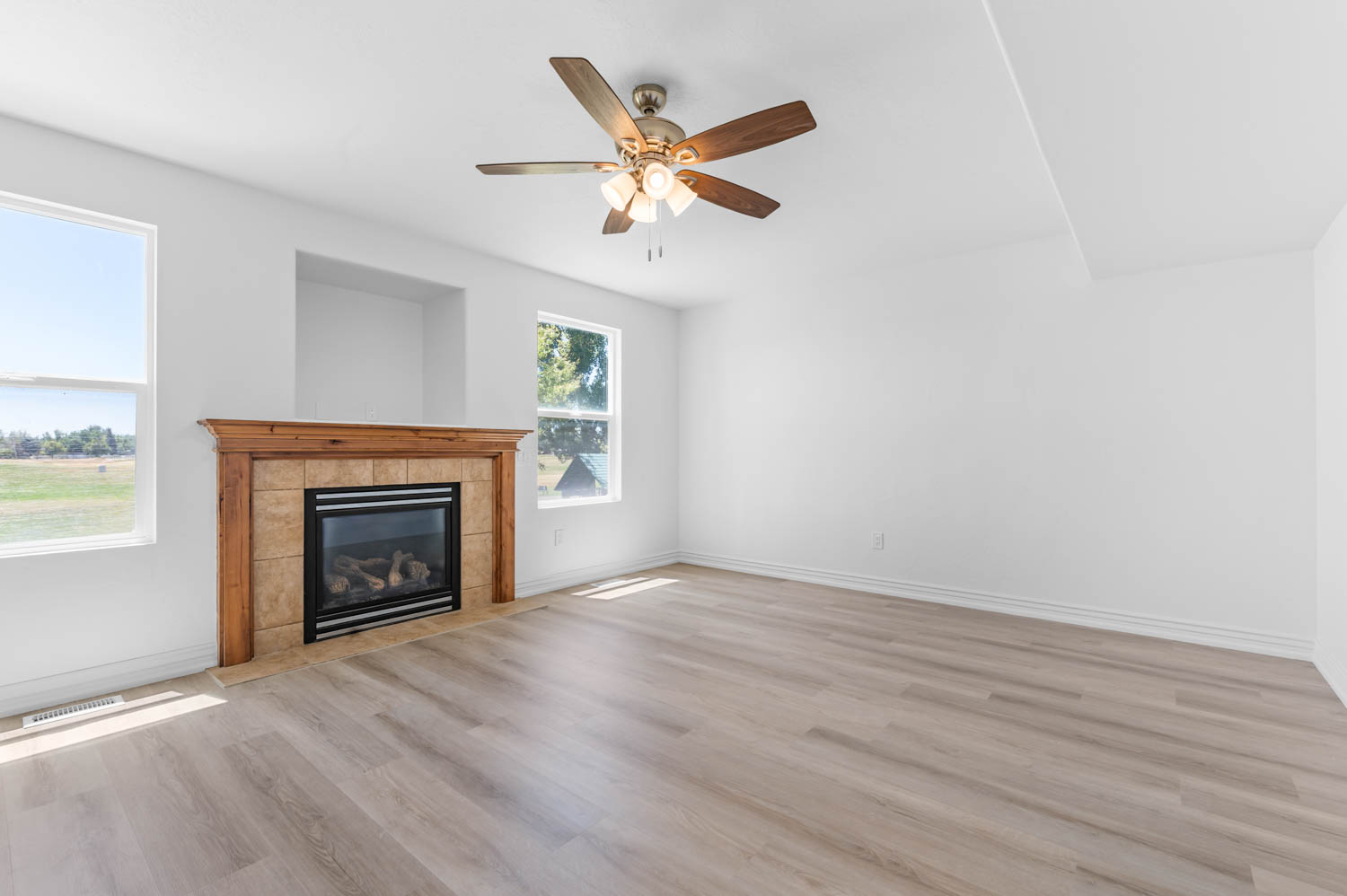 Living area featuring a fireplace with a wood mantle and tile surround, wood-finish flooring, a ceiling fan with integrated lighting, and multiple windows
