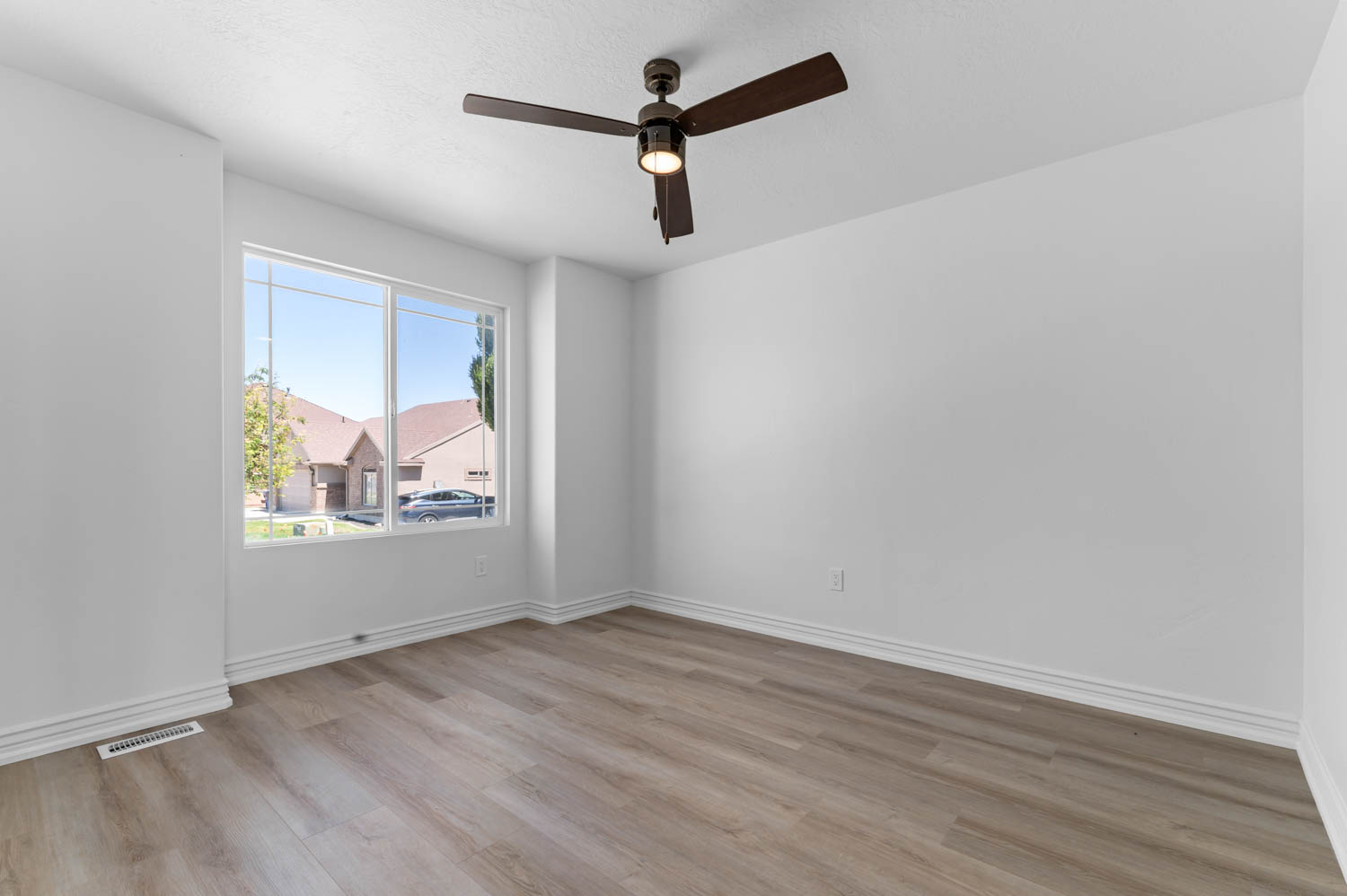 Bright room featuring a large window, a ceiling fan with integrated lighting, wood-finish flooring, white walls, and white baseboards