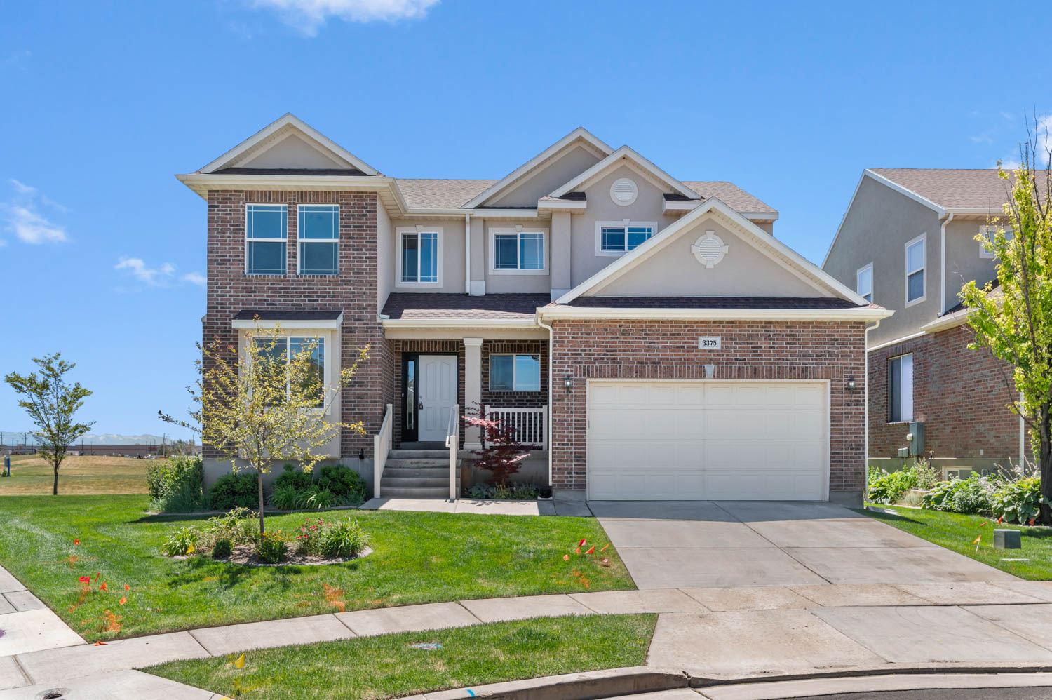 Two-story residence featuring a brick and stucco exterior, an attached two-car garage, an inviting covered porch, a concrete driveway, and a front lawn with foundational landscaping
