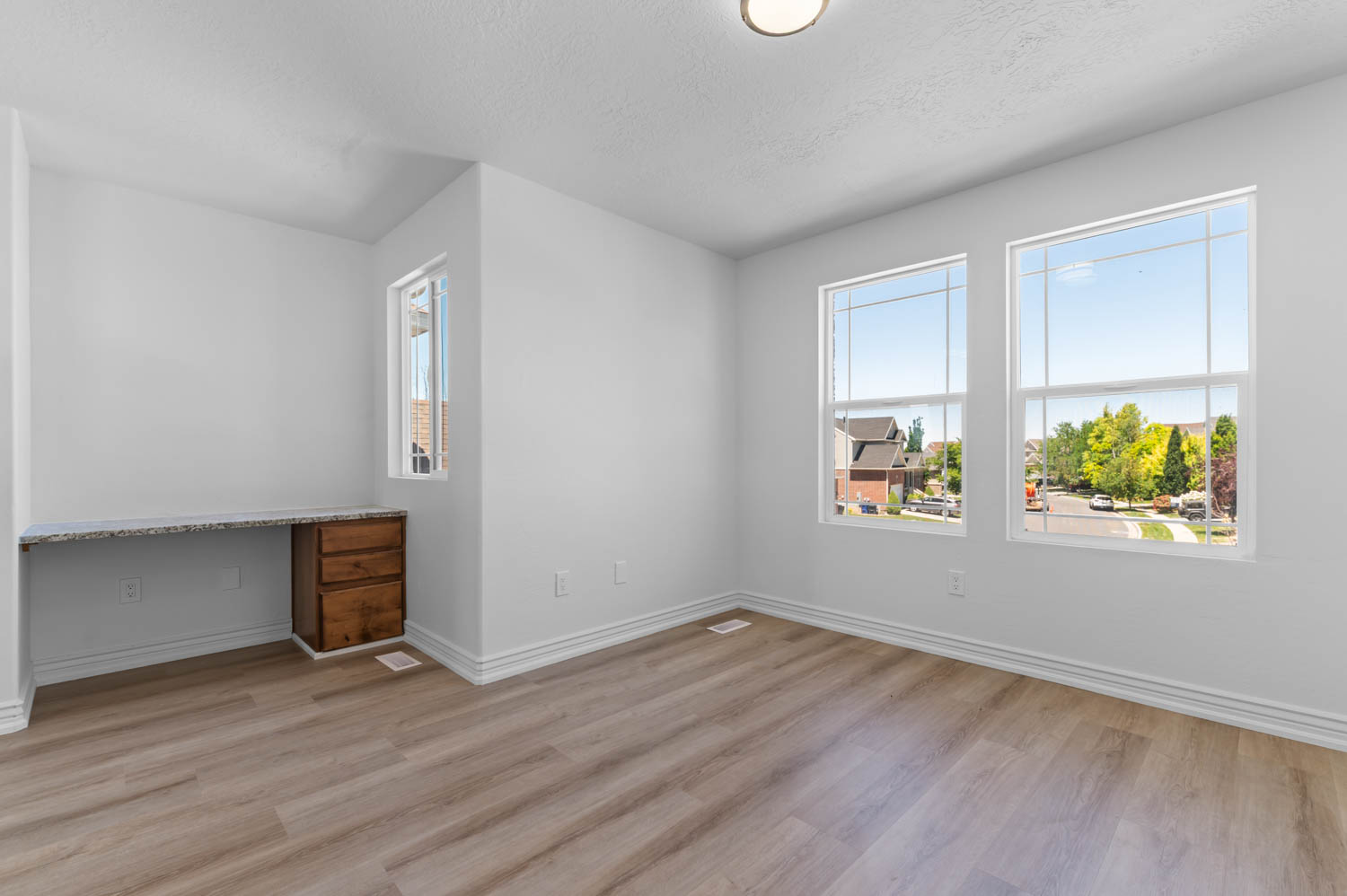 Room featuring multiple windows, wood-finish flooring, white baseboards, and a built-in desk with a stone-finish countertop and wooden cabinetry