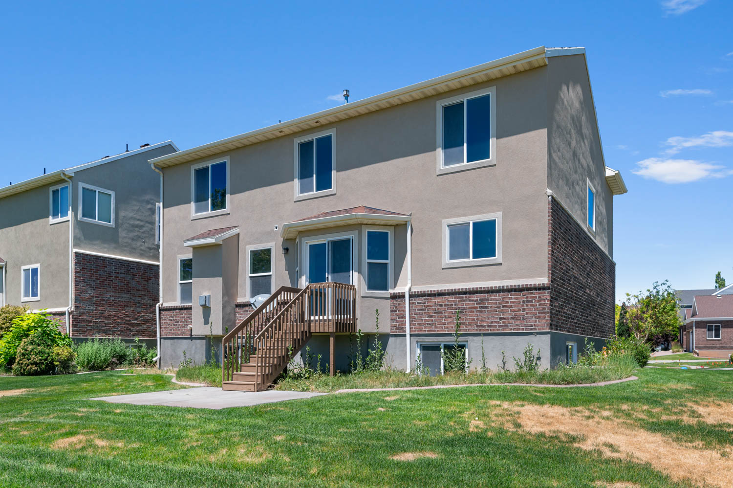 Rear exterior featuring stucco and brick facade, a ground-level patio, and an elevated wood deck with stairs