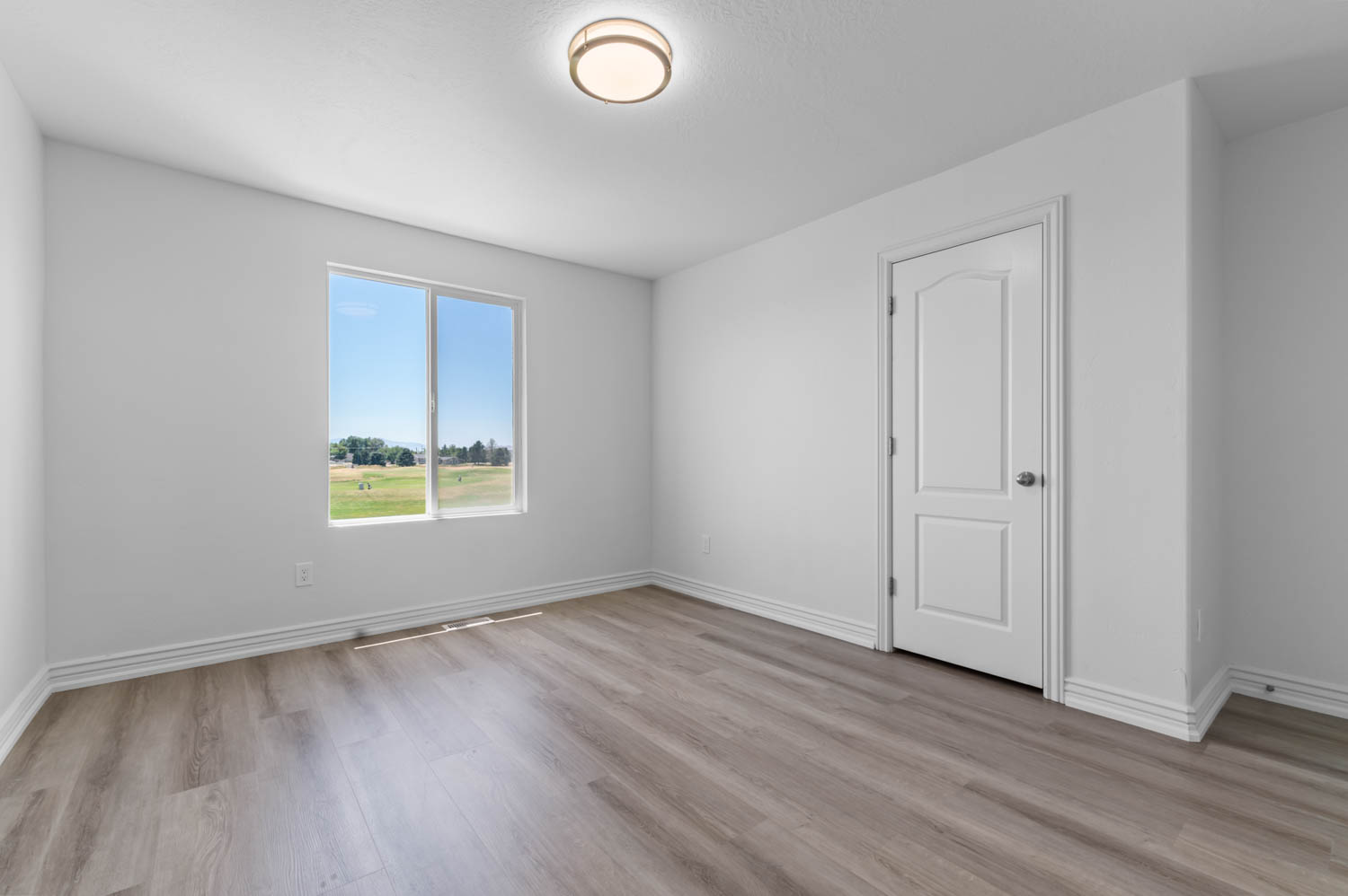 Interior room featuring wood-finish flooring, a white paneled door, and a large window