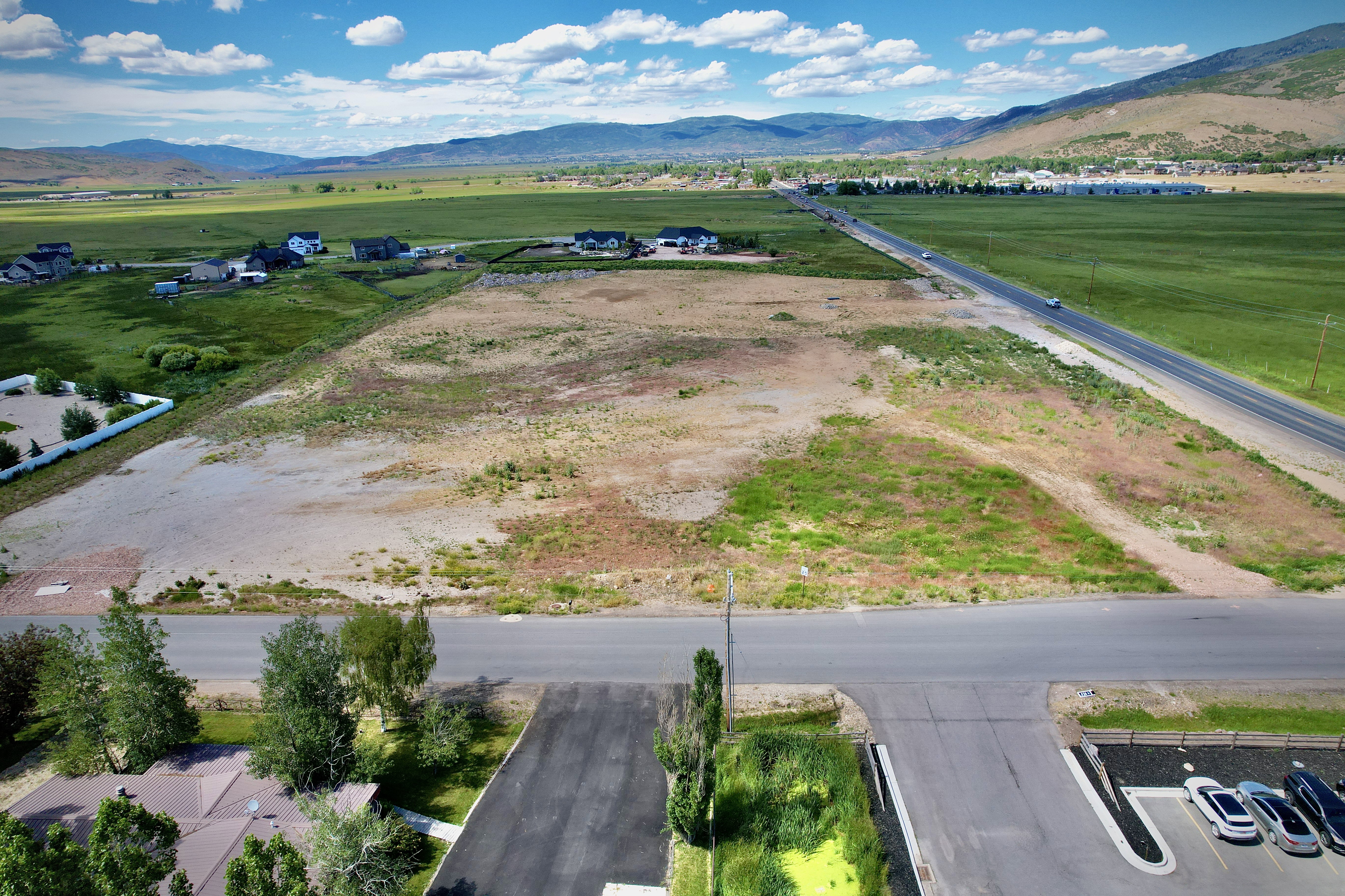 Expansive undeveloped land featuring a paved road, mountain backdrop, and scattered residential properties in the background