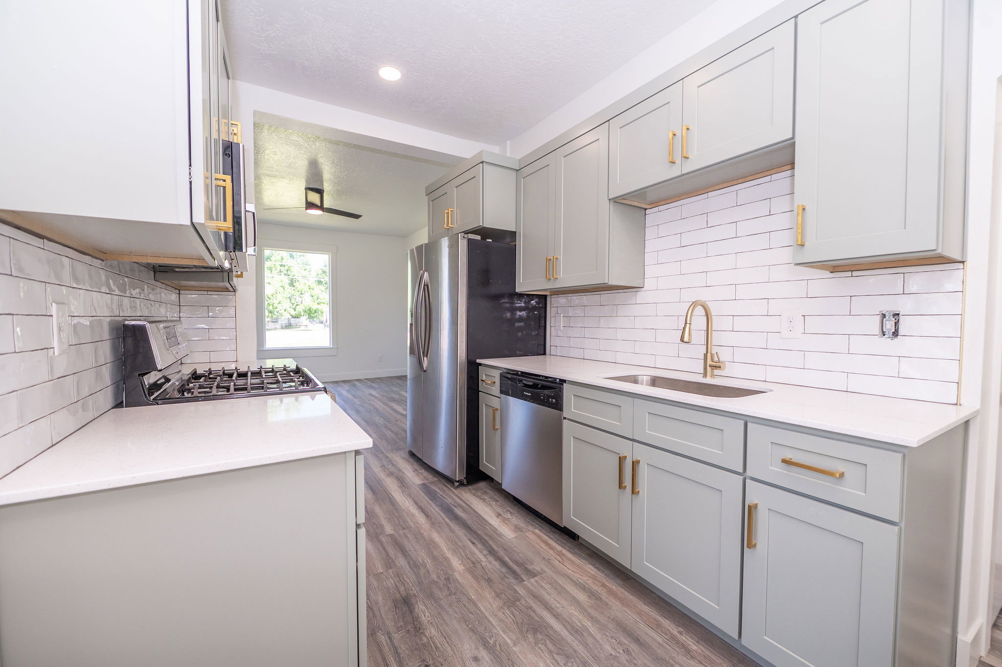 Modern kitchen featuring light gray cabinetry with gold-tone hardware, white subway tile backsplash, white countertops, and stainless steel appliances