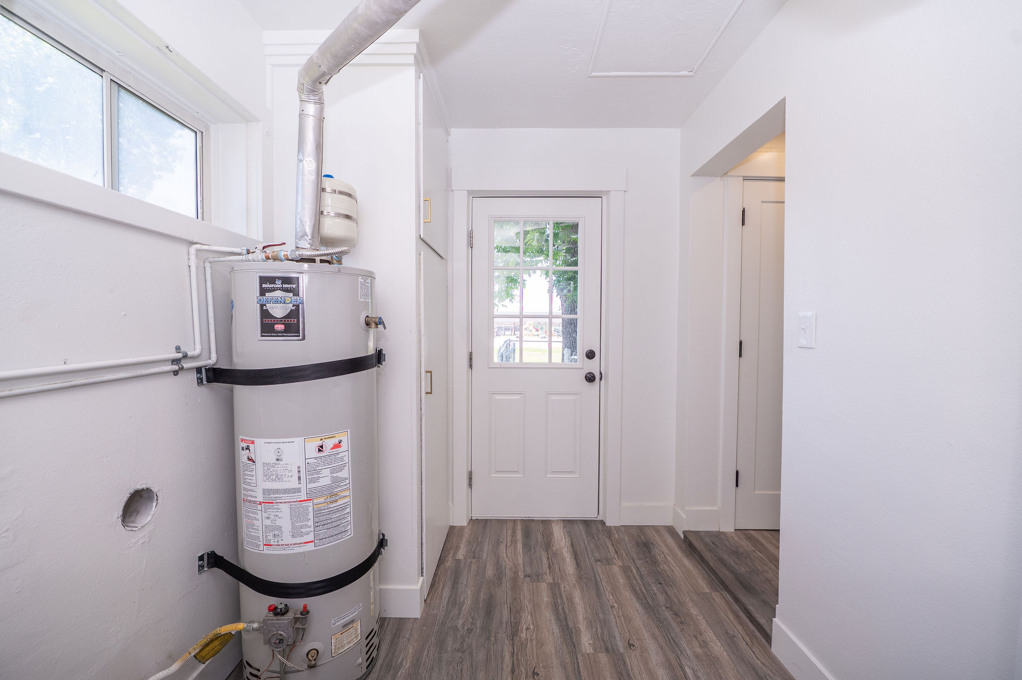 Utility room featuring a water heater, a window with exterior visibility, wood-finish flooring, a white paneled door with glass inserts, and a white interior door