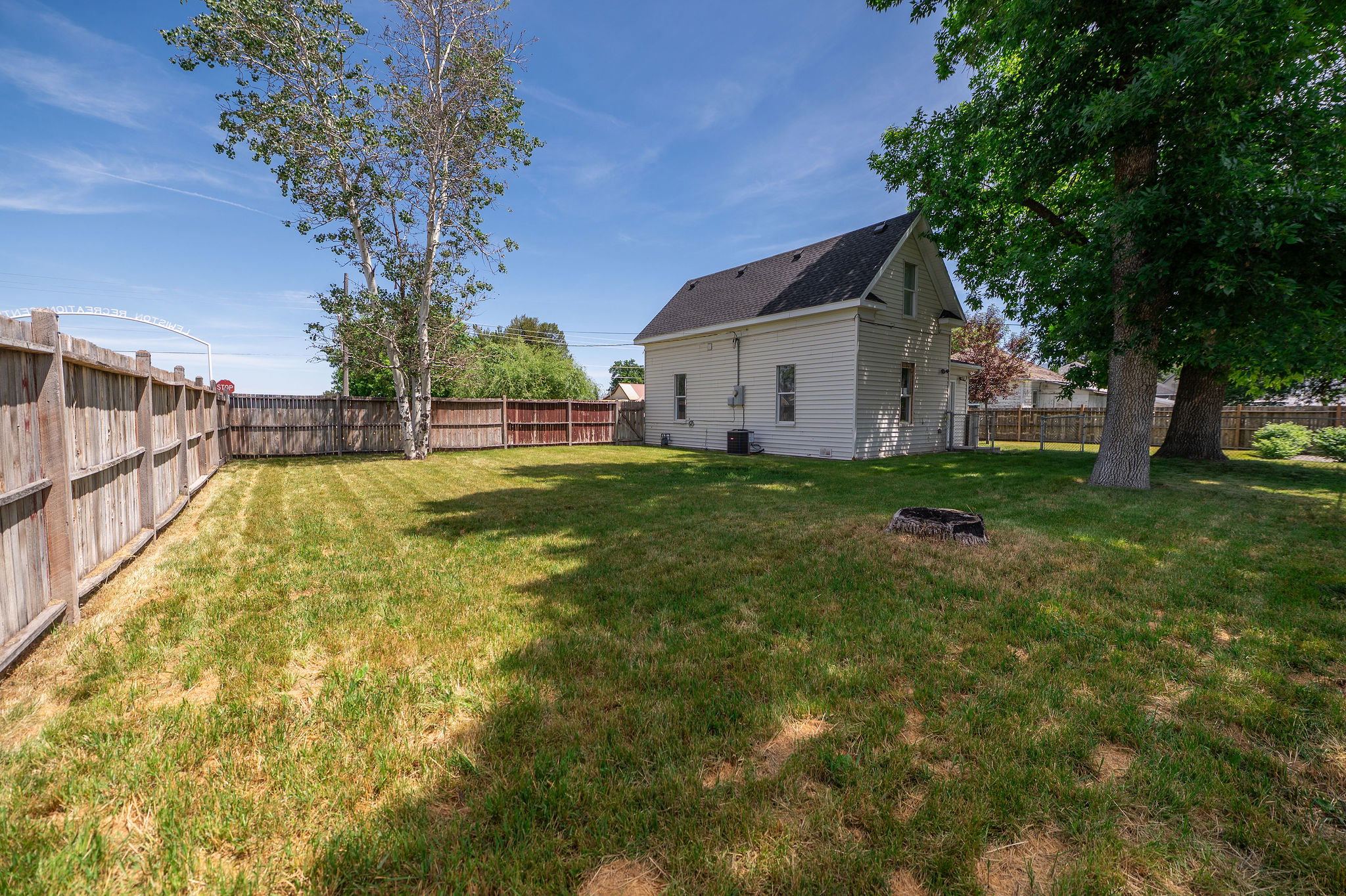 Expansive fenced yard featuring a white siding exterior, mature trees, and a dark shingle roof
