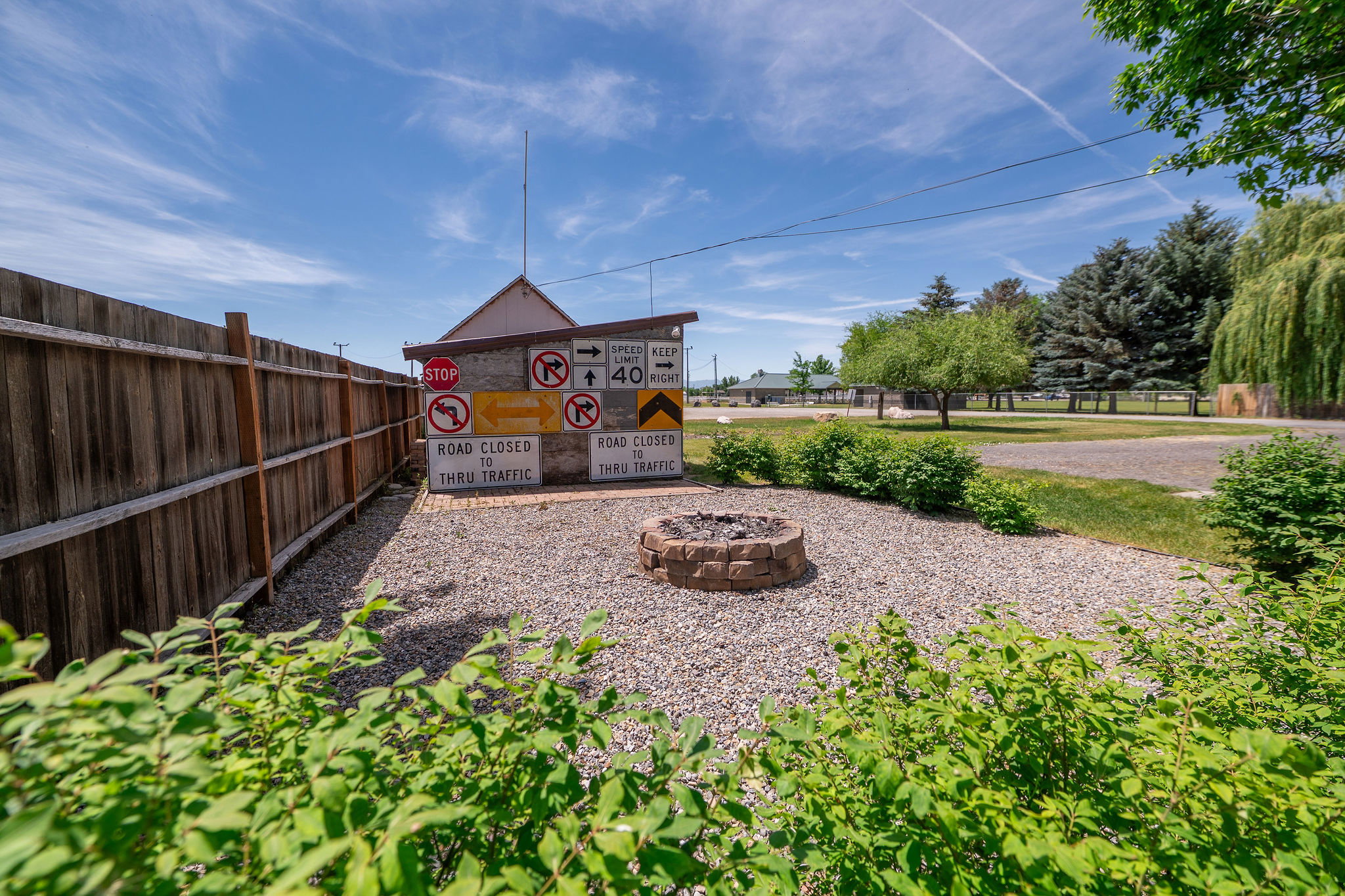 Gravel outdoor area featuring a stone-built fire pit, wood privacy fencing, and green landscaping