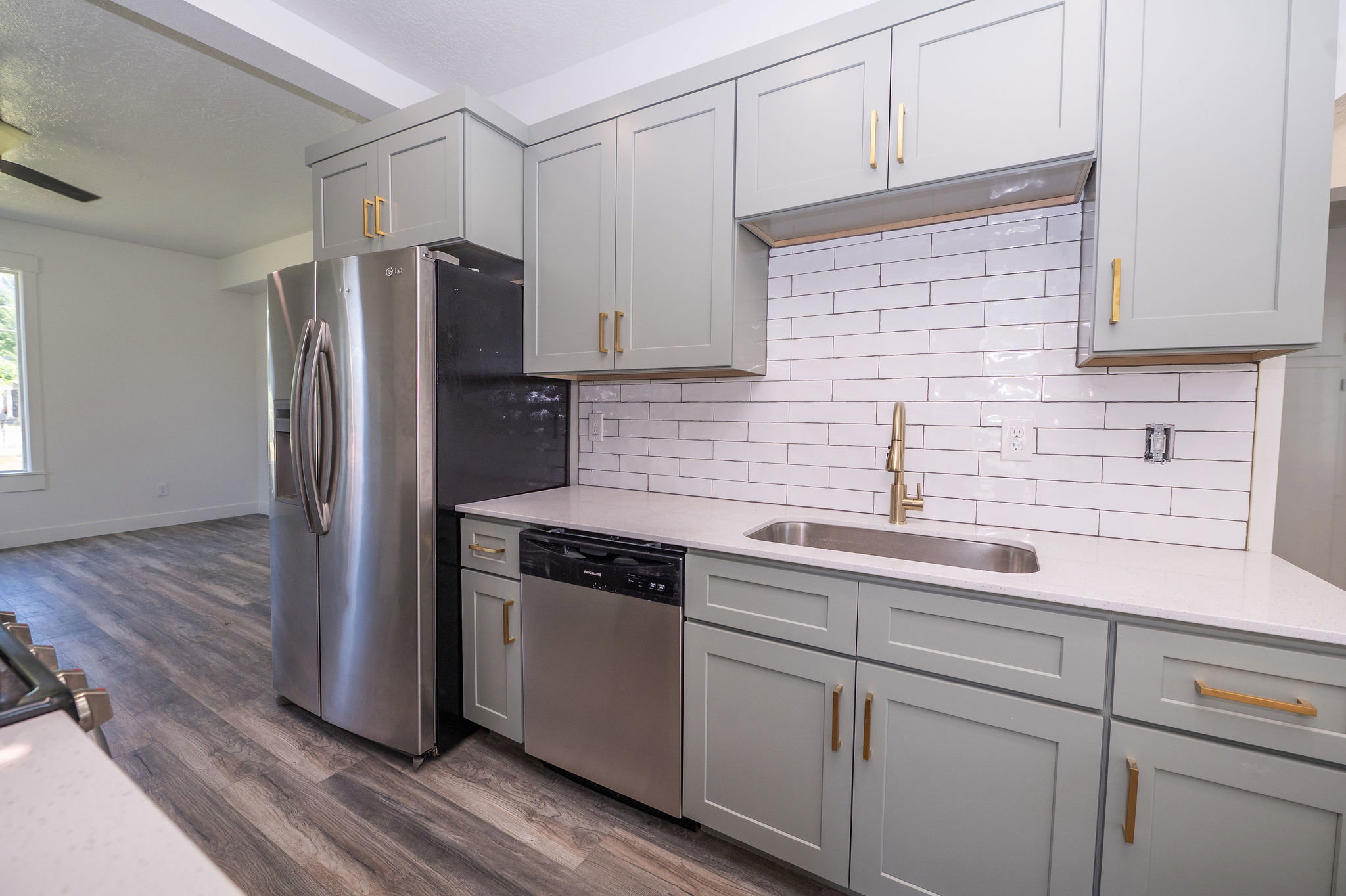 Modern kitchen featuring sage green shaker cabinetry with gold-tone hardware, white subway tile backsplash, and light-toned countertops