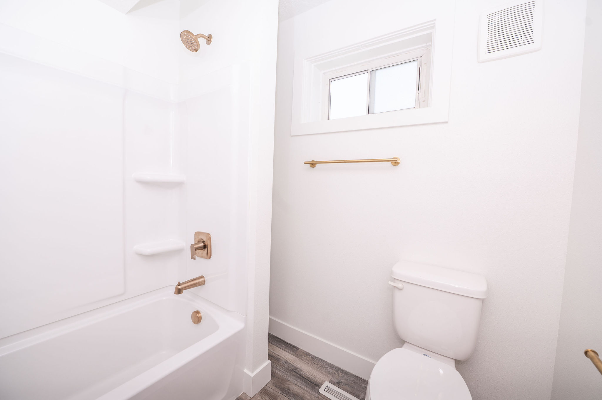 Full bathroom featuring a white tub/shower combination with integrated shelving, brushed bronze fixtures, and a white toilet