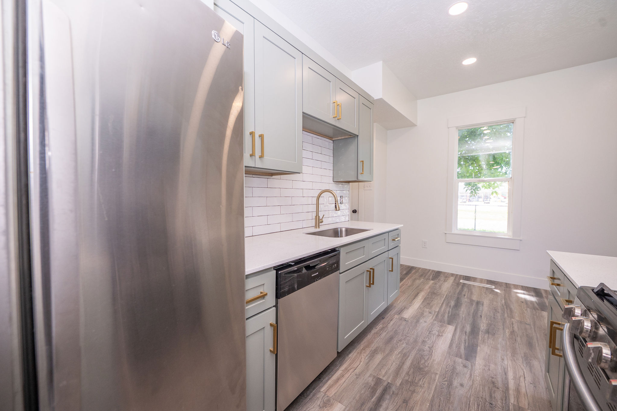 Modern kitchen featuring stainless steel appliances, light-toned cabinetry with gold-finish hardware, quartz countertops, and a subway tile backsplash