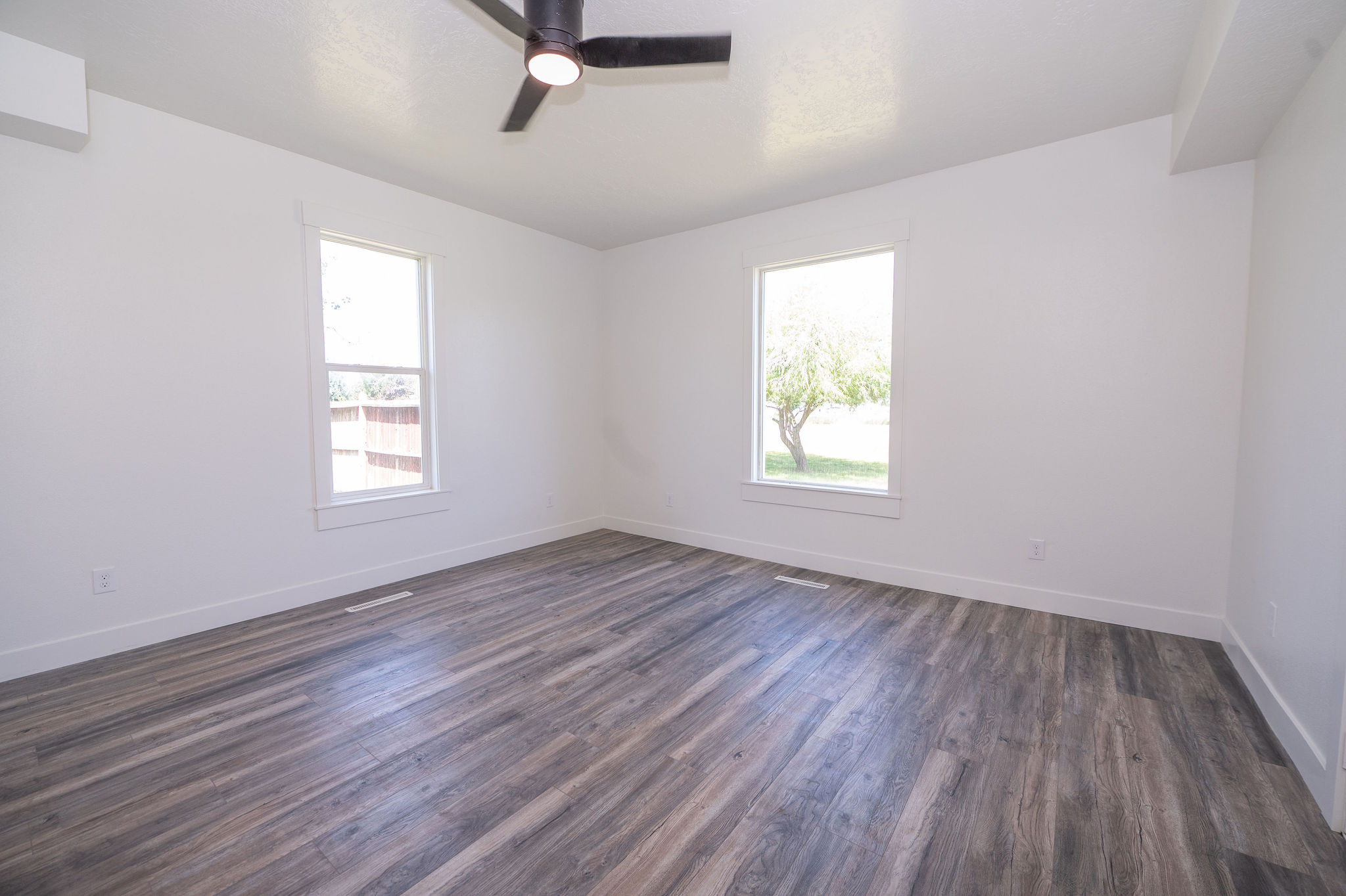 Spacious room featuring wood-finish flooring, white walls, and bright windows