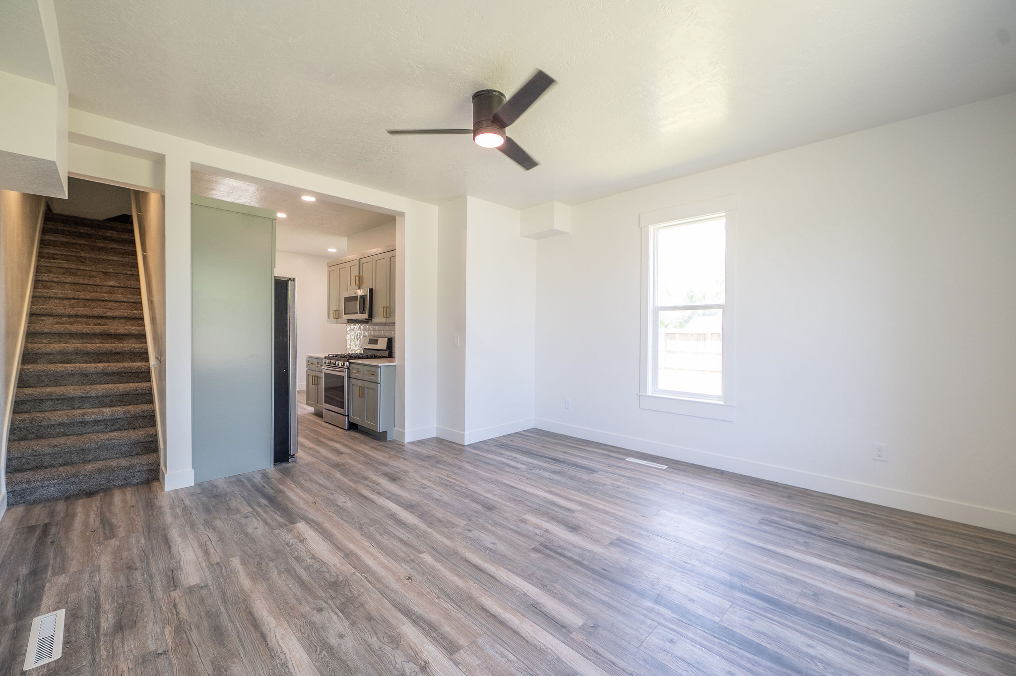 Spacious living area featuring wood-finish flooring and a ceiling fan with integrated lighting