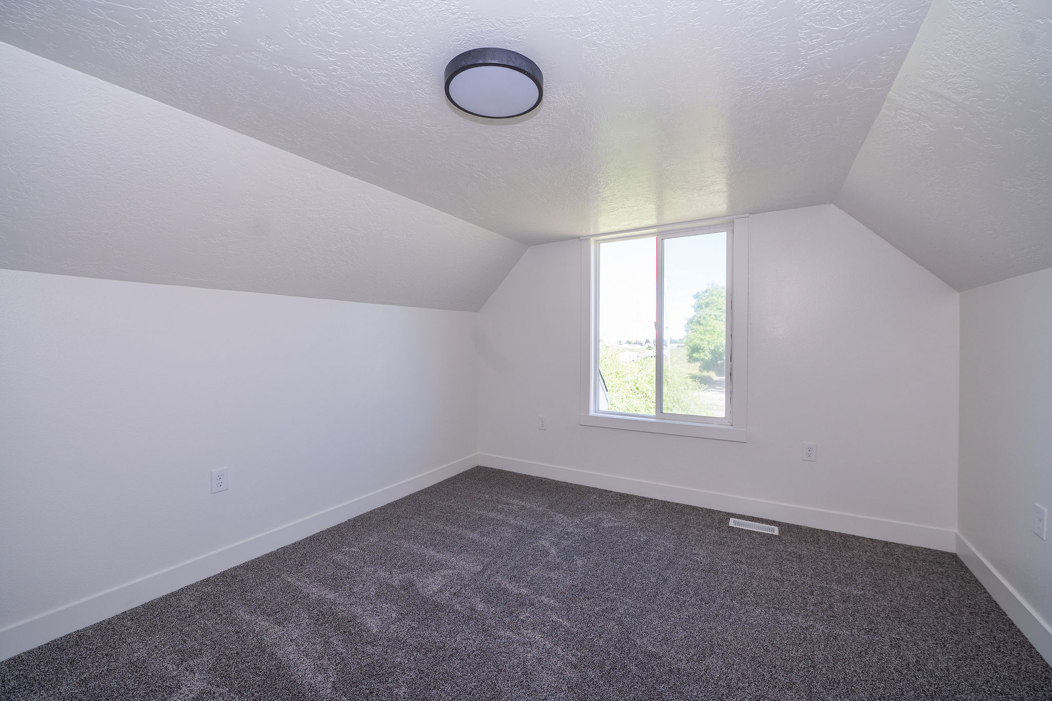 Room featuring a white-framed window, textured carpeting, sloped ceilings, and a flush-mount ceiling light