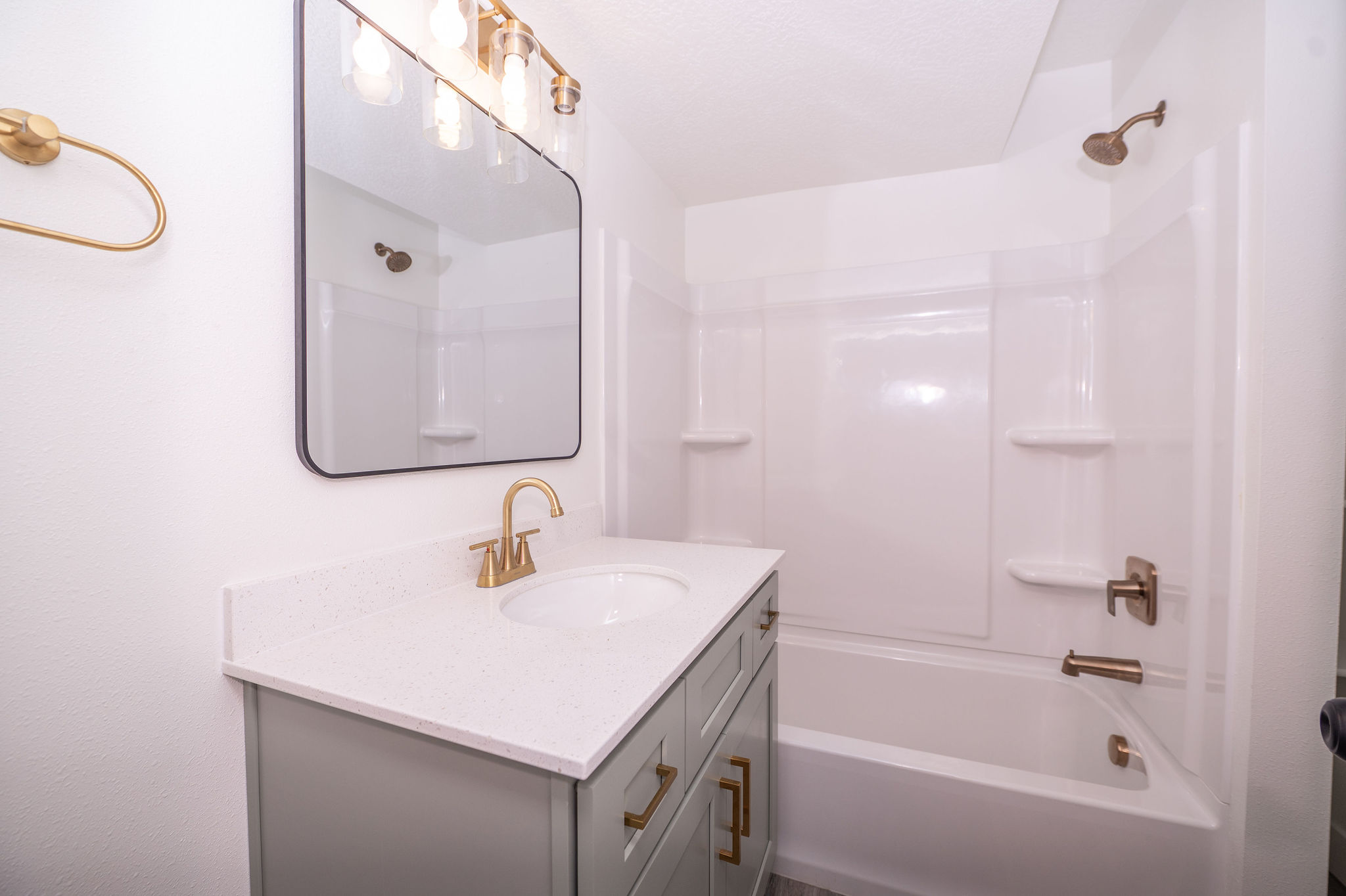 Bathroom featuring a modern vanity with light green cabinetry and gold-finish hardware, a white countertop, and a rectangular mirror with black trim