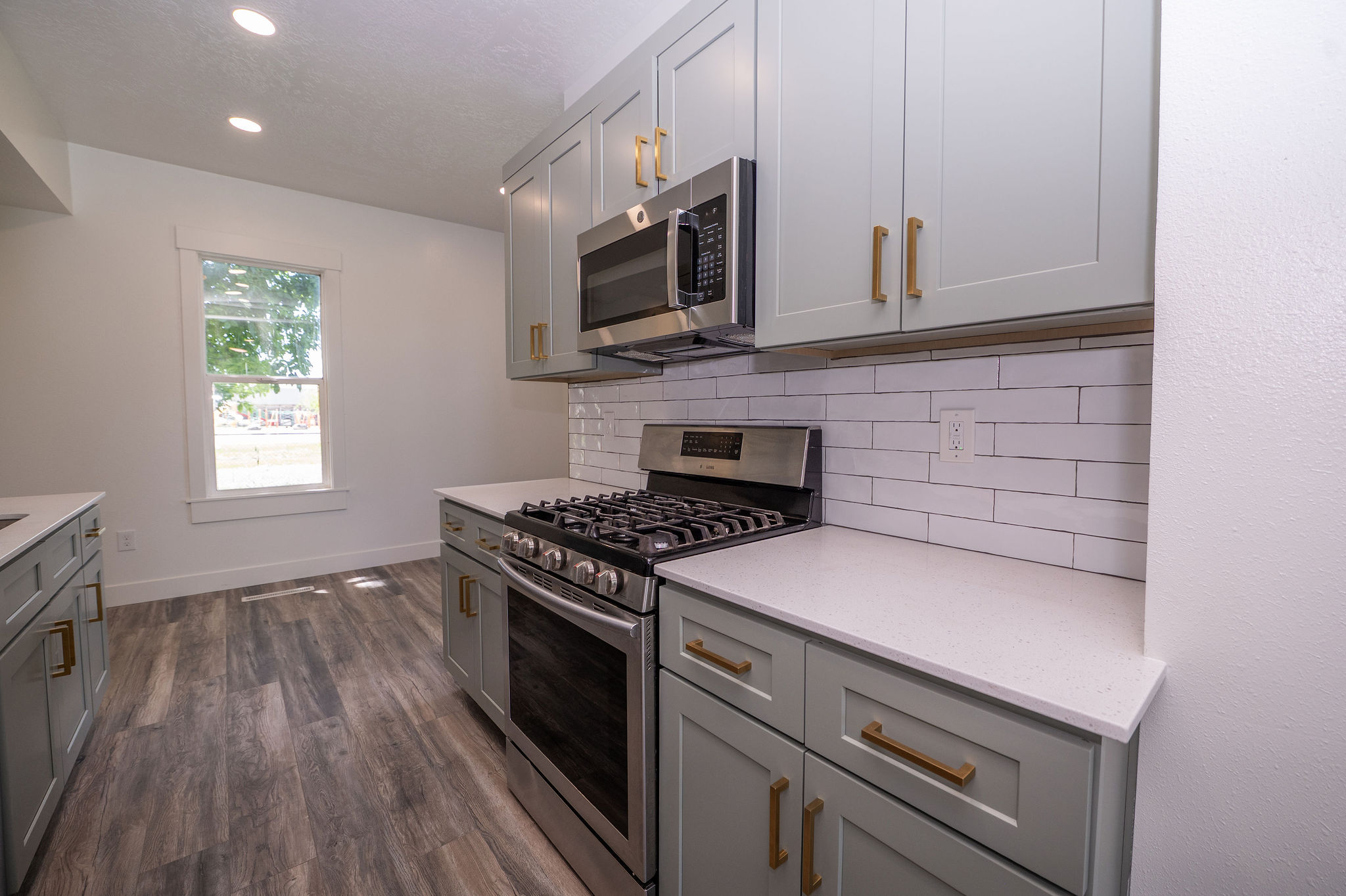 Kitchen featuring light gray cabinetry with gold-tone hardware, white countertops, stainless steel appliances, and a white subway tile backsplash
