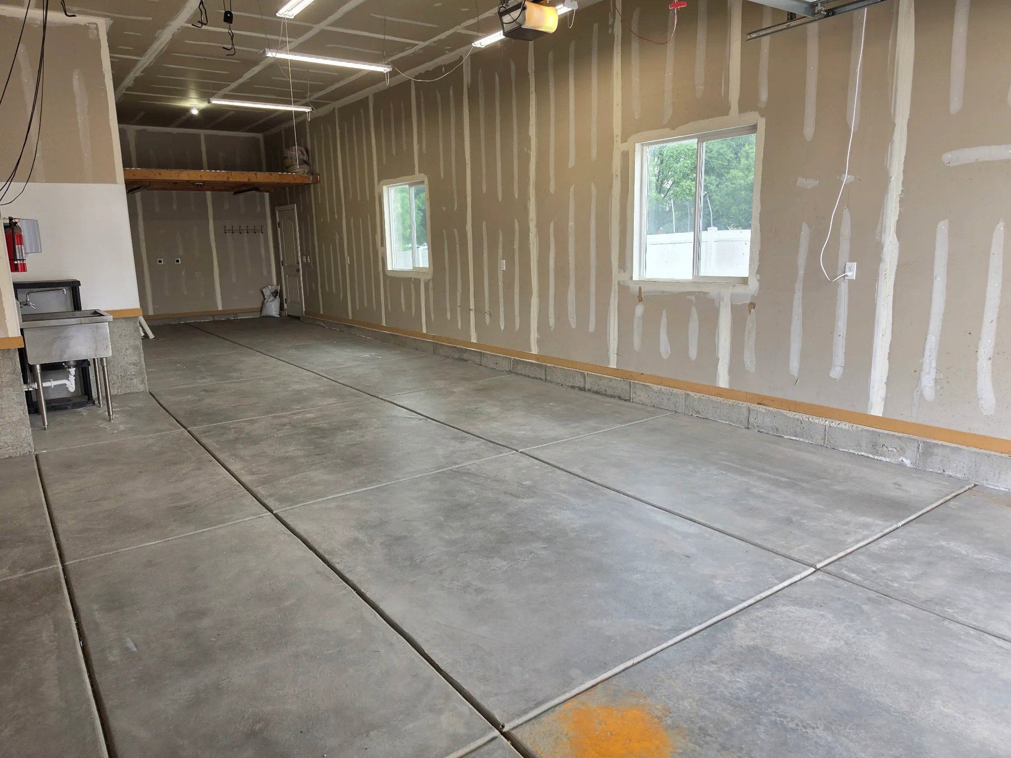 Spacious garage featuring a concrete floor, two windows providing natural light, overhead fluorescent lighting, an integrated utility sink, and a high storage shelf