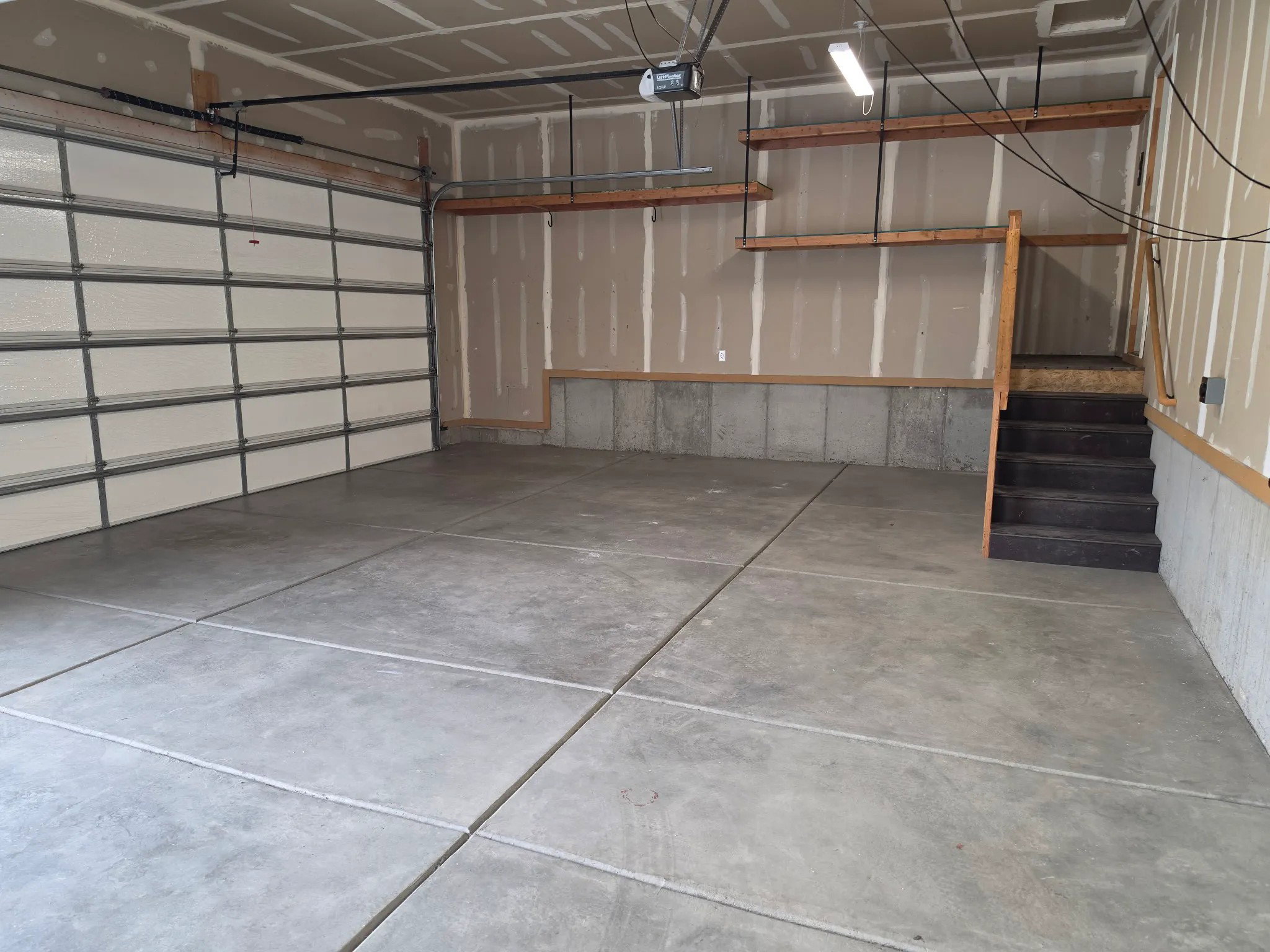 Two-car garage featuring a concrete floor, overhead lighting, integrated shelving, and a built-in staircase