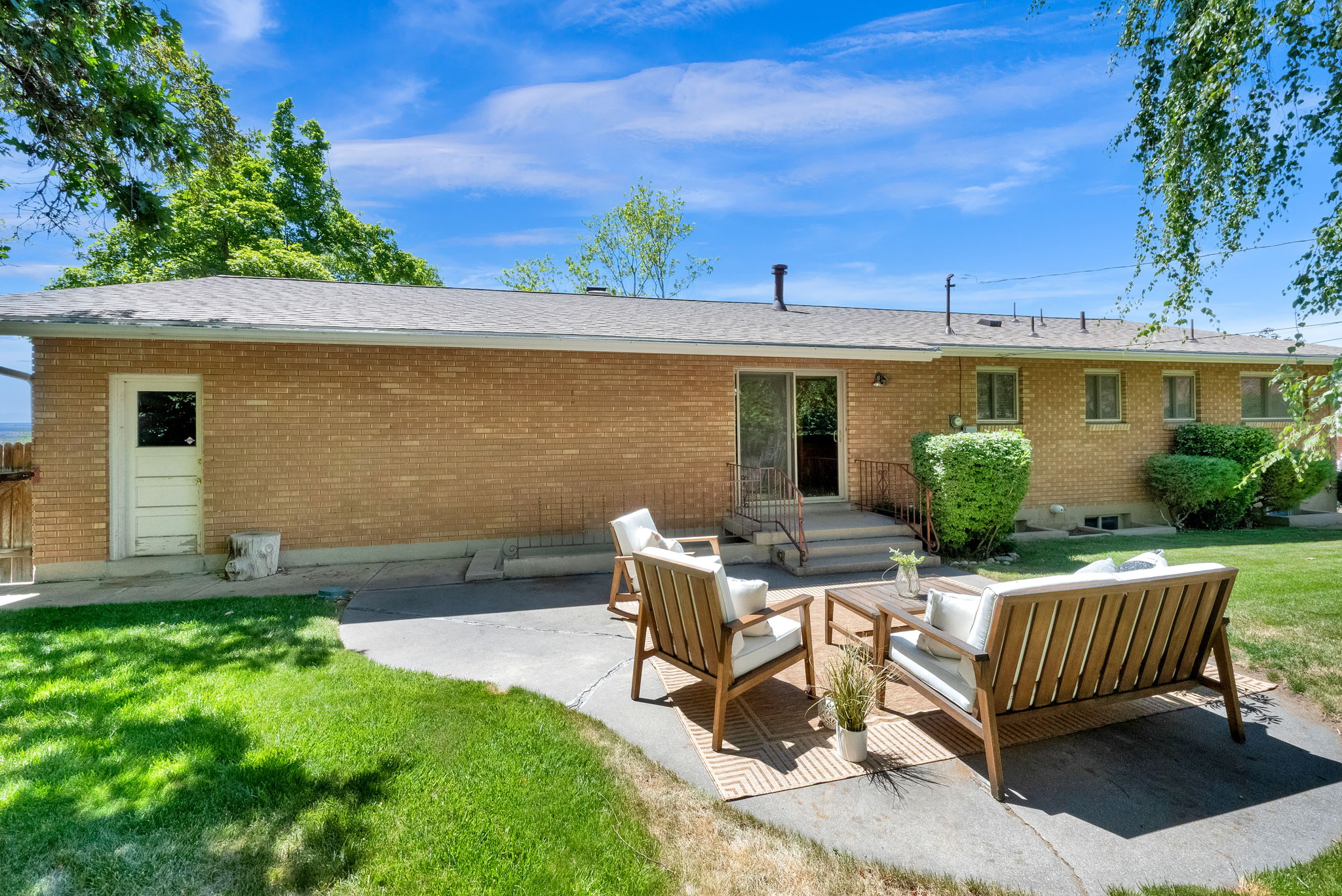 Expansive backyard featuring a manicured lawn, established shade trees, and a concrete patio