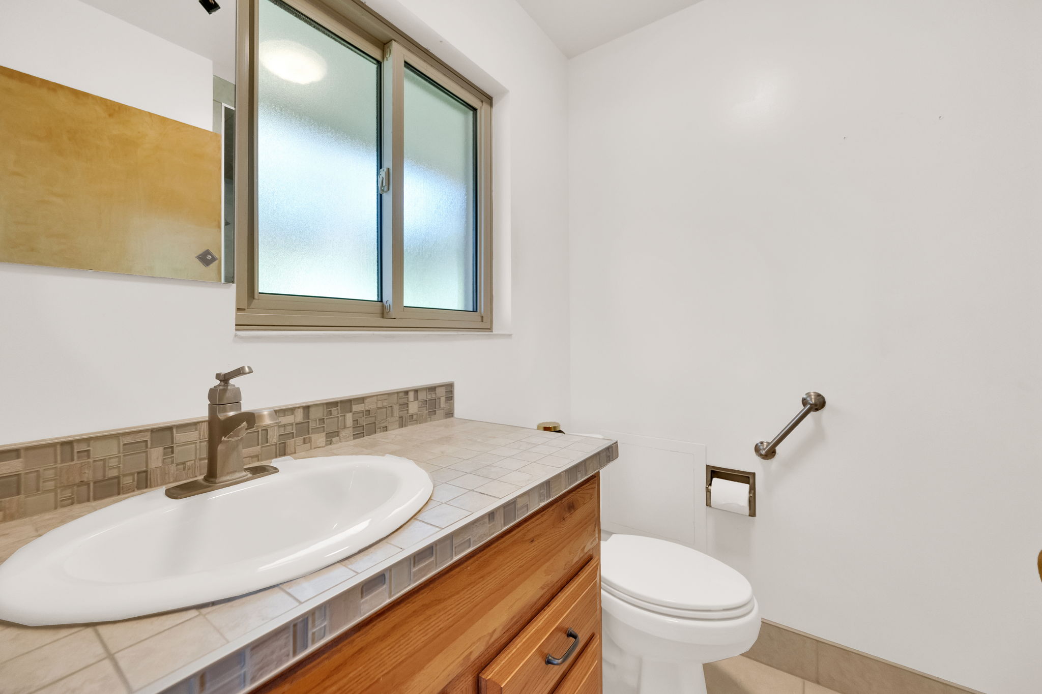Bathroom vanity with a tiled countertop, tiled shower, and brushed nickel faucet
