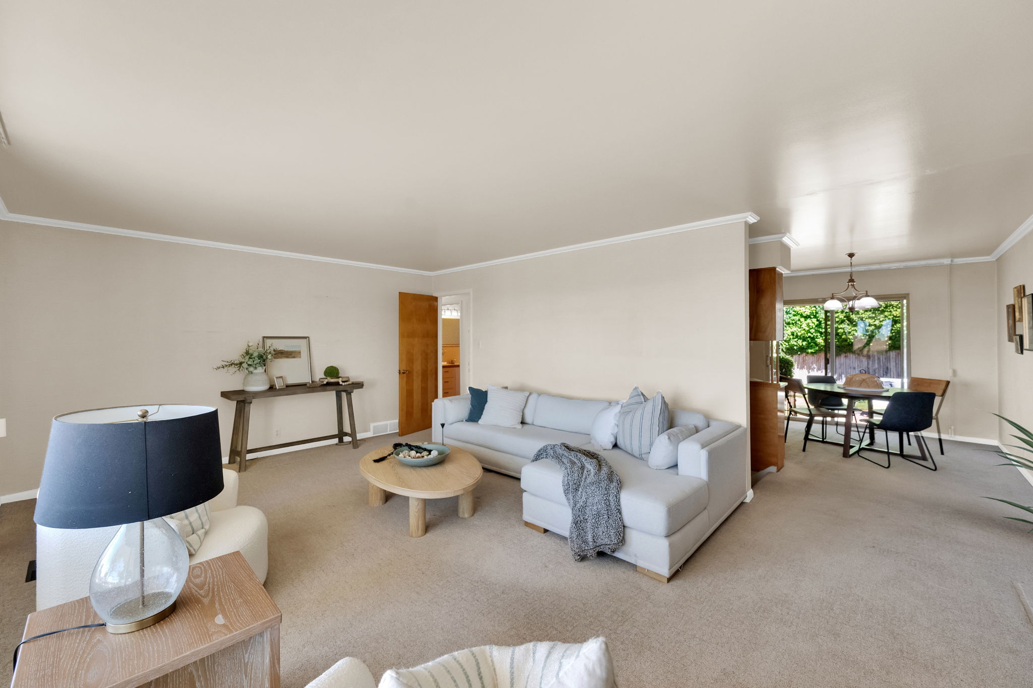 Carpeted living space with crown molding open to dining
