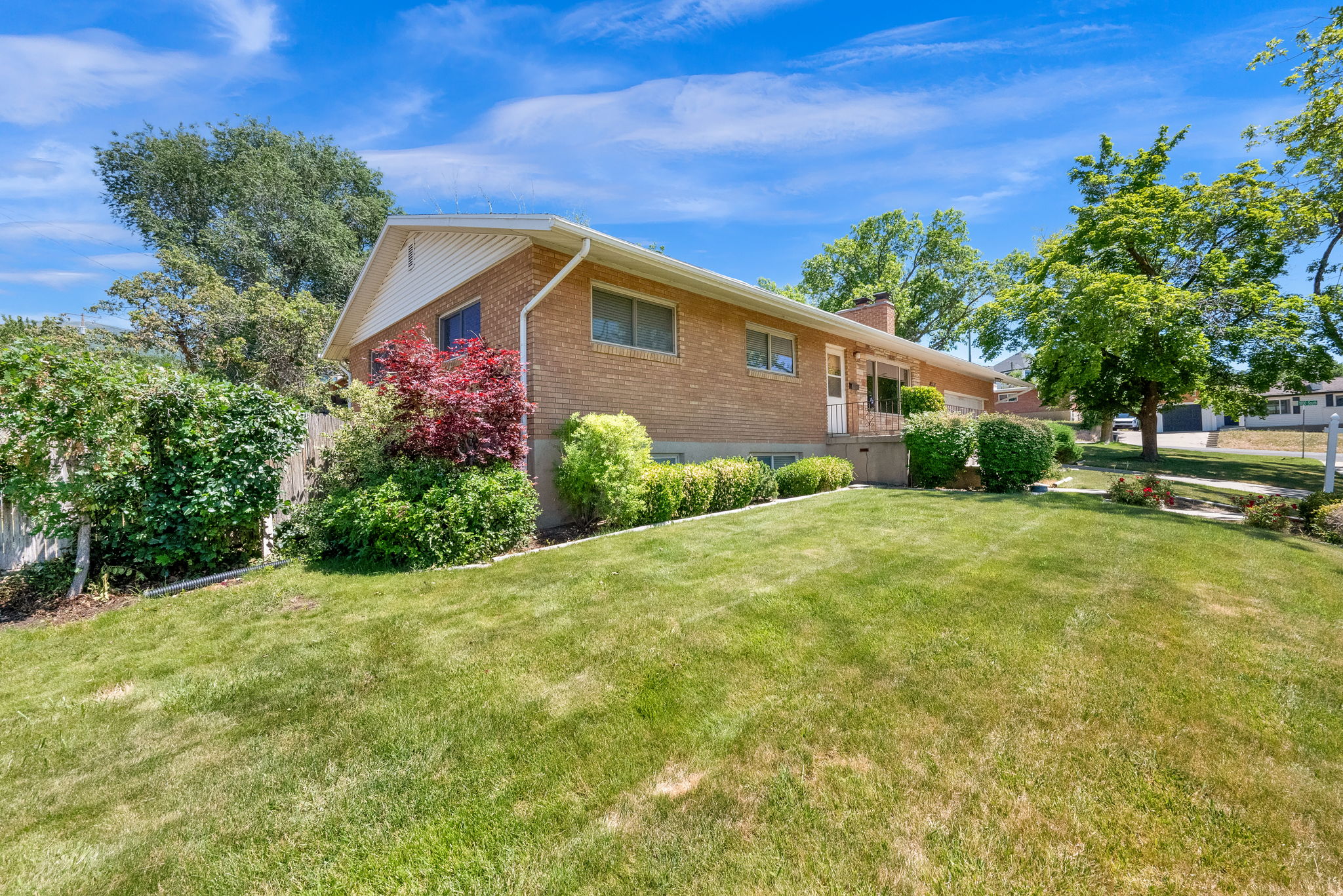 Brick exterior residence featuring a covered front entry, mature landscaping, a sloped lawn