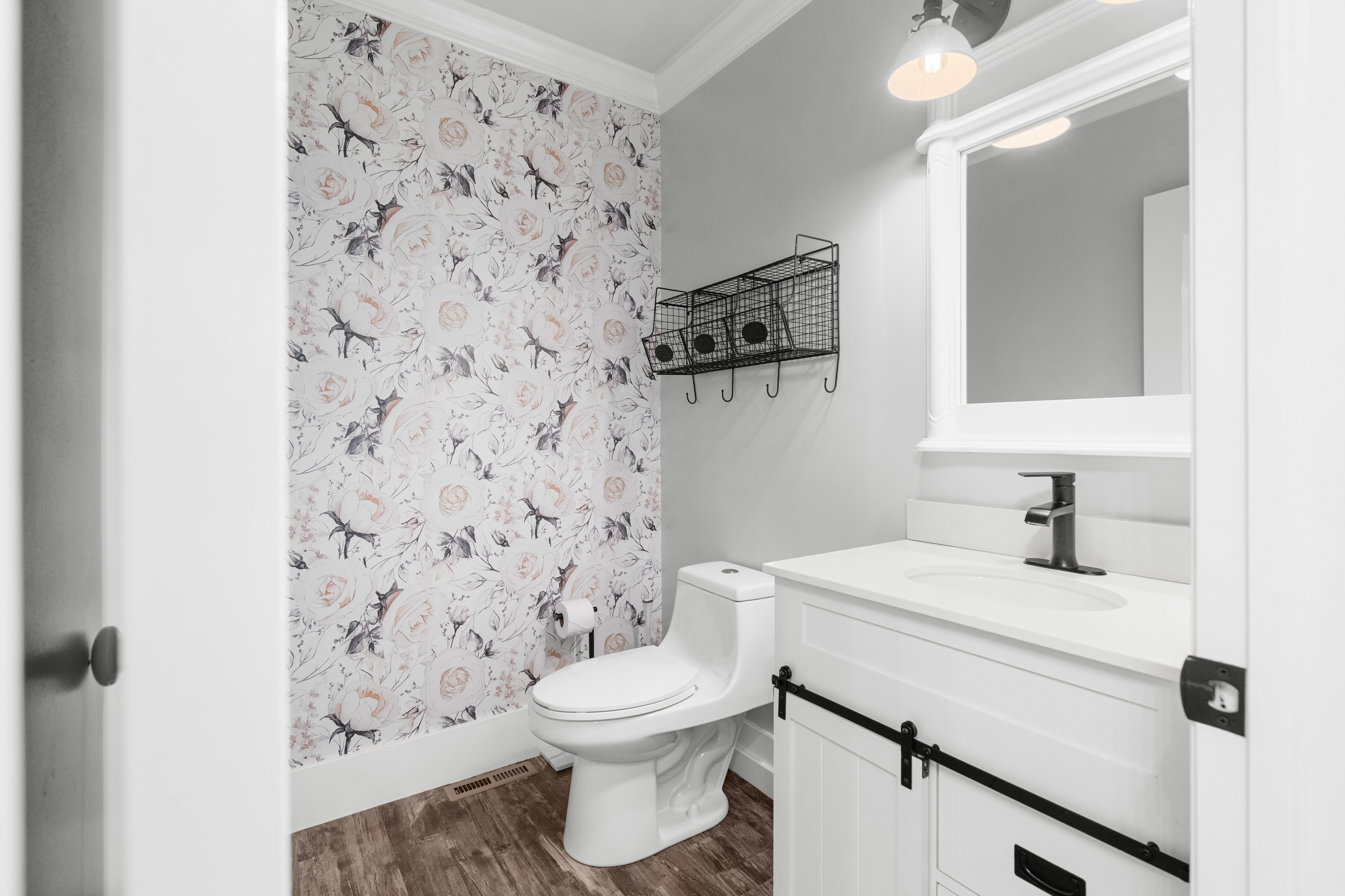 Half bath room featuring botanical print wallpaper, LVP flooring, white vanity with, matte black faucet, and a wall-mounted mirror with integrated lighting