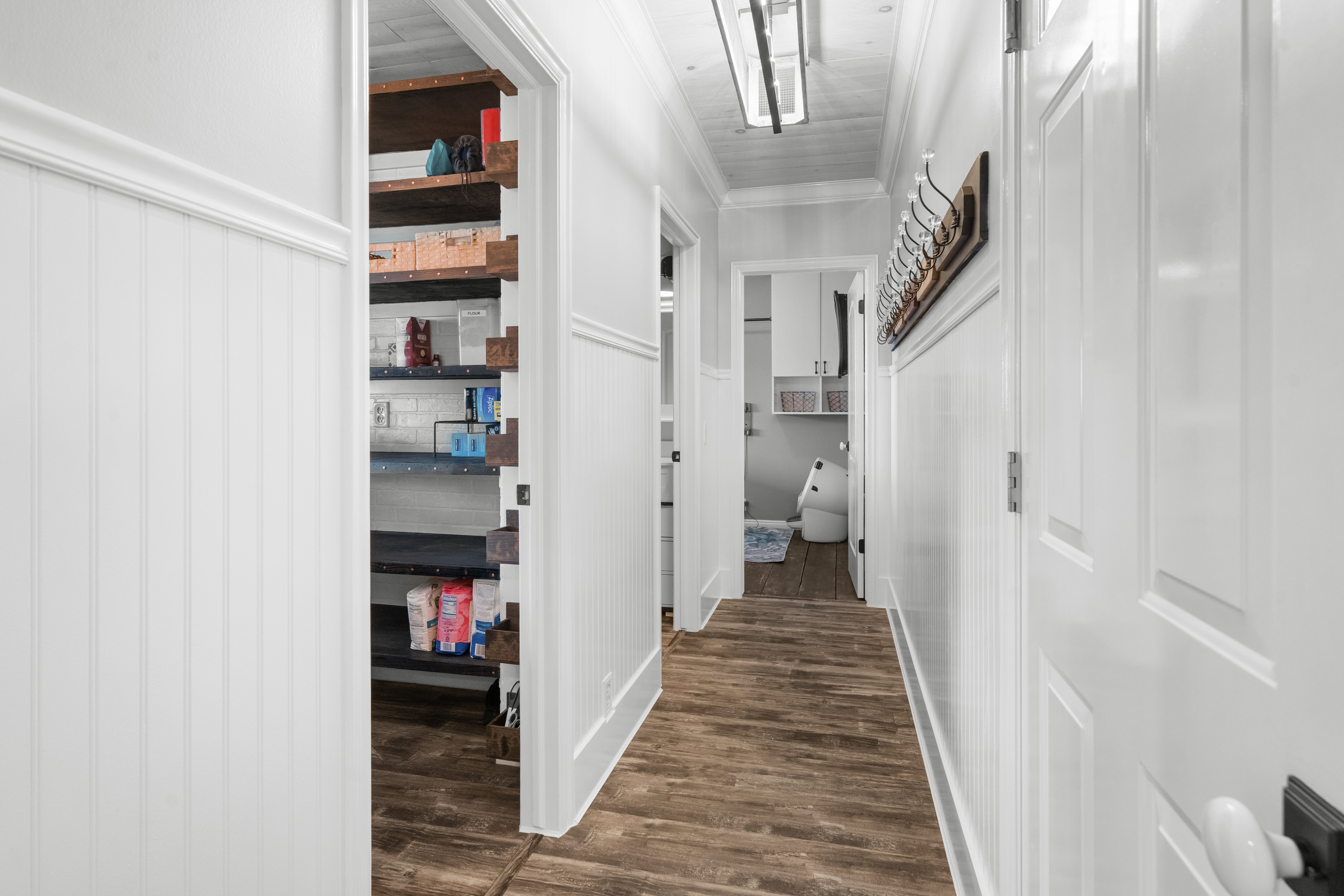 Hardwood-style flooring throughout a hallway featuring white wainscoting and crown molding