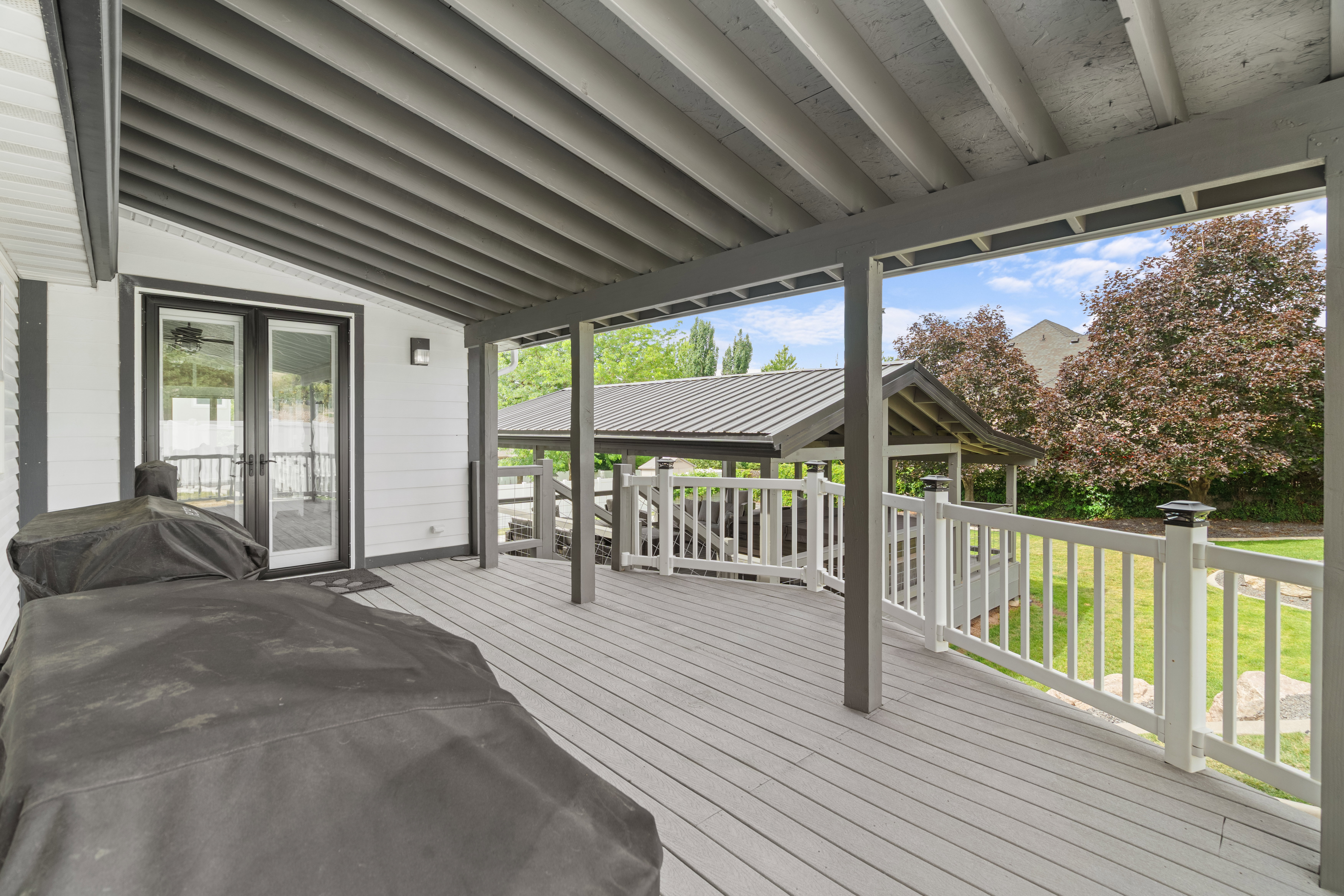 Additional covered deck conveniently located off the great room, featuring low-maintenance composite decking, classic white railings, and a striking dark gray slatted ceiling that creates a stylish outdoor living space