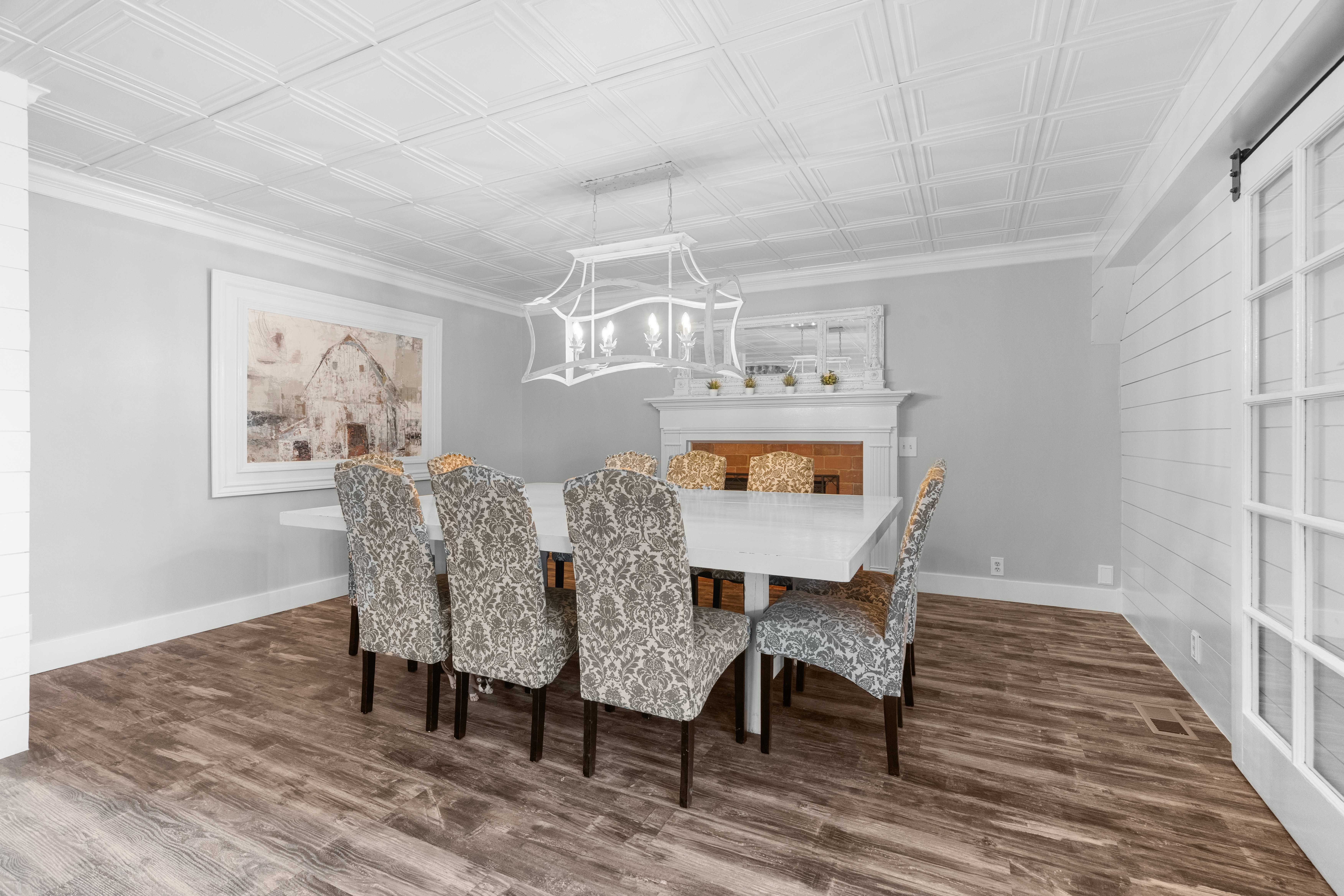 Spacious formal dining area featuring LPV  flooring, a white coffered ceiling, a decorative fireplace with mantel, and a sliding barn door with glass panels