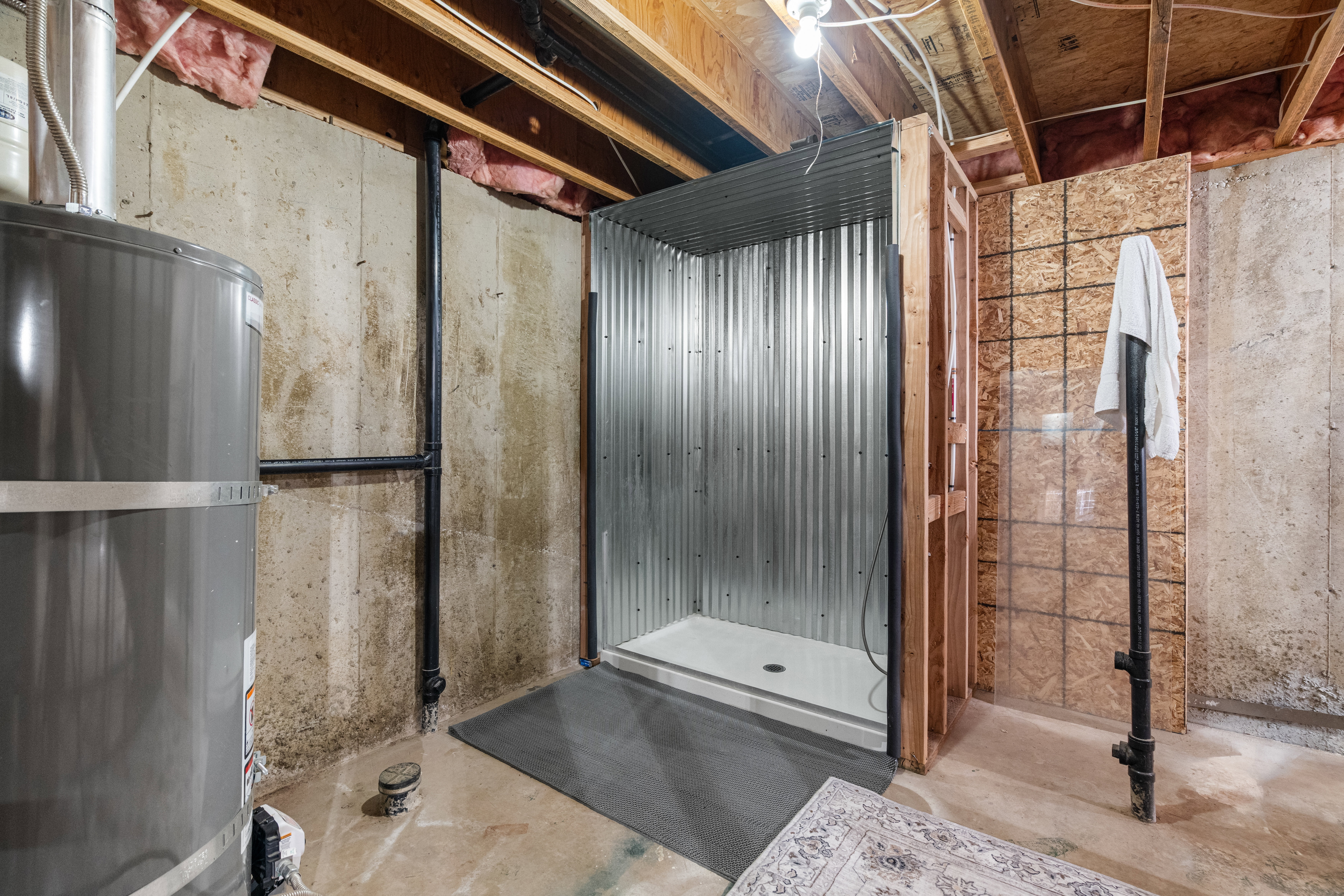 Functional utility area with concrete flooring, updated water heater, and dedicated space for future expansion. Includes a built-in pet washing station and an unfinished shower enclosure, offering flexibility for additional customization and utility