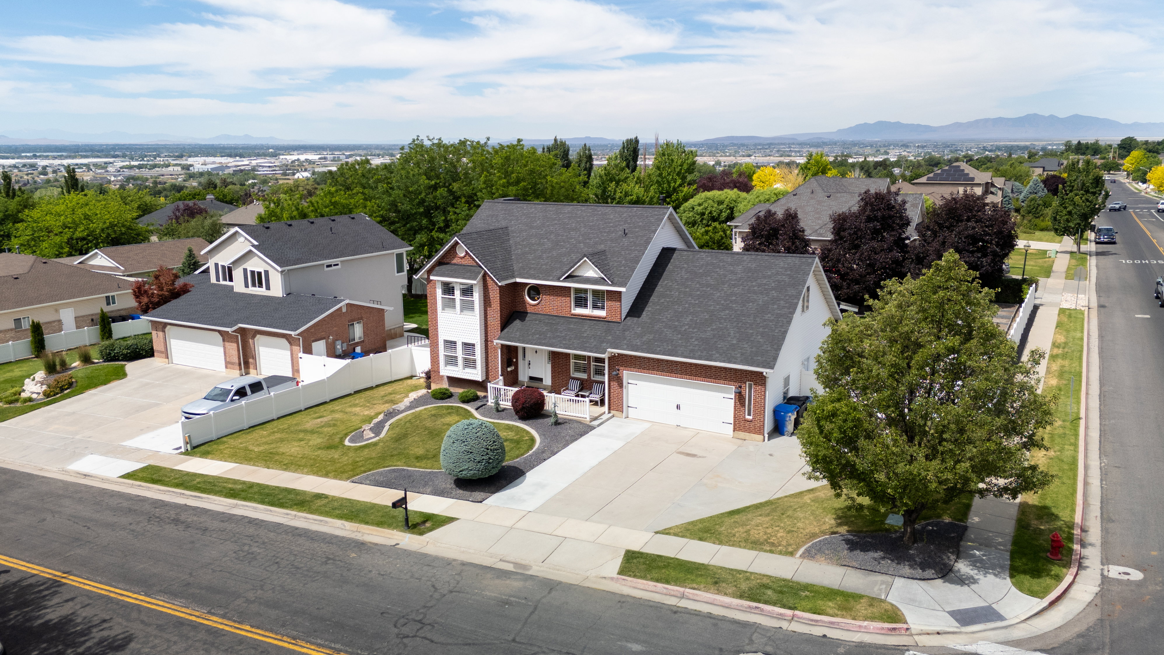 Aerial view of our two-story residence featuring a brick facade with white trim, a dark shingle roof, and an attached two-car garage