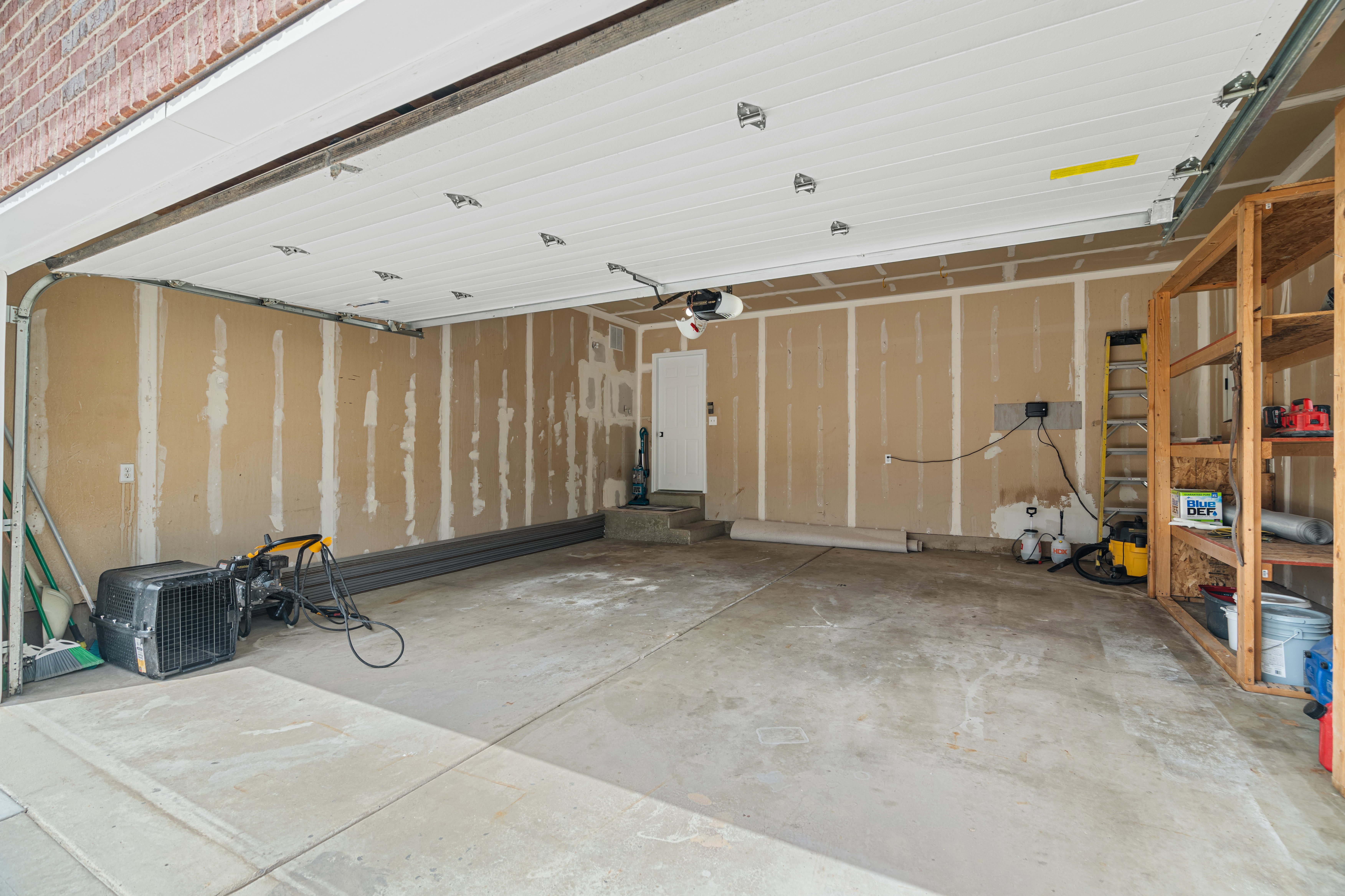 Spacious garage featuring a concrete floor, exposed drywall, and an overhead garage door with custom built shelving