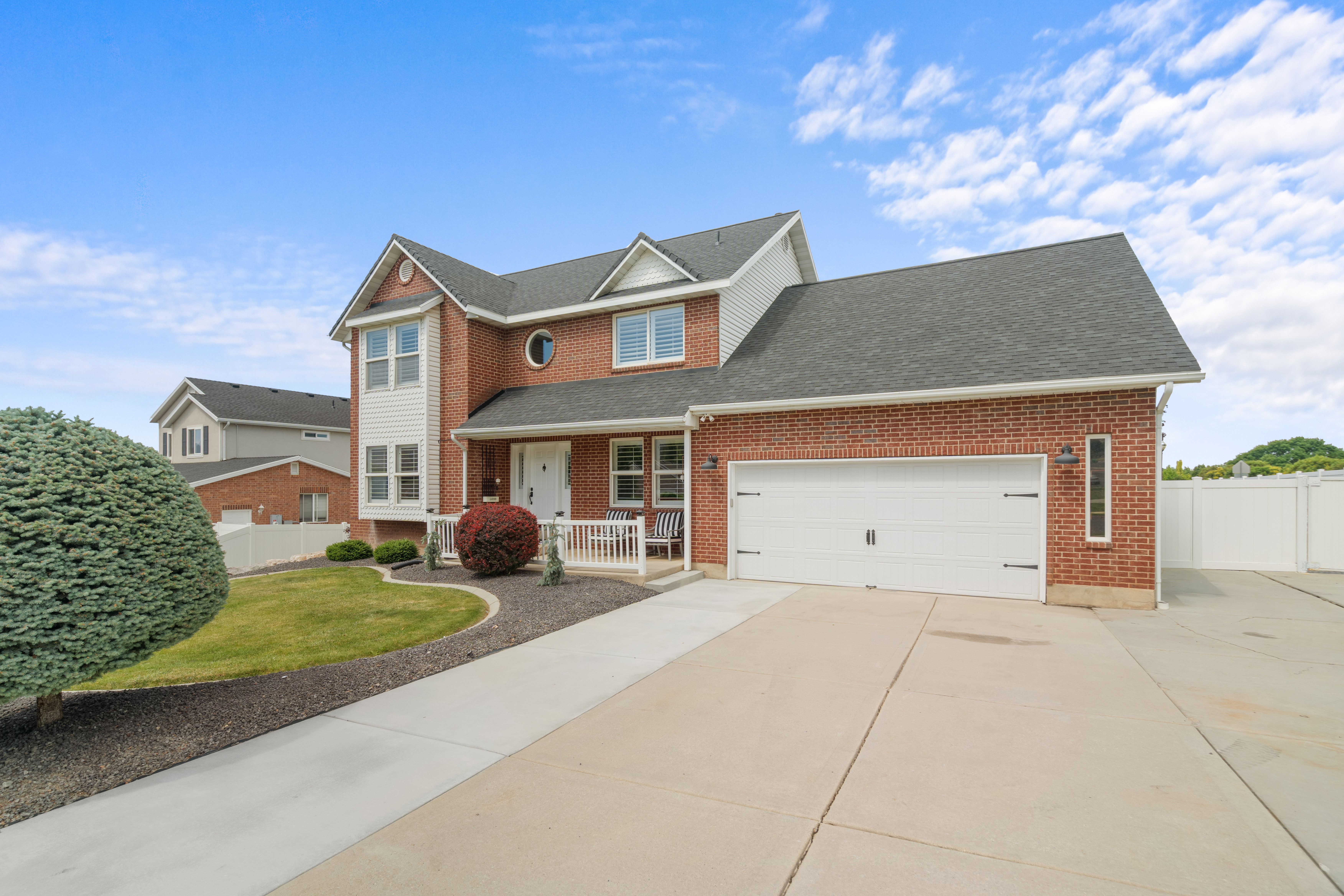 Brick and siding exterior featuring a multi-gable roofline, attached two-car garage, concrete driveway, and a covered front porch with white railings