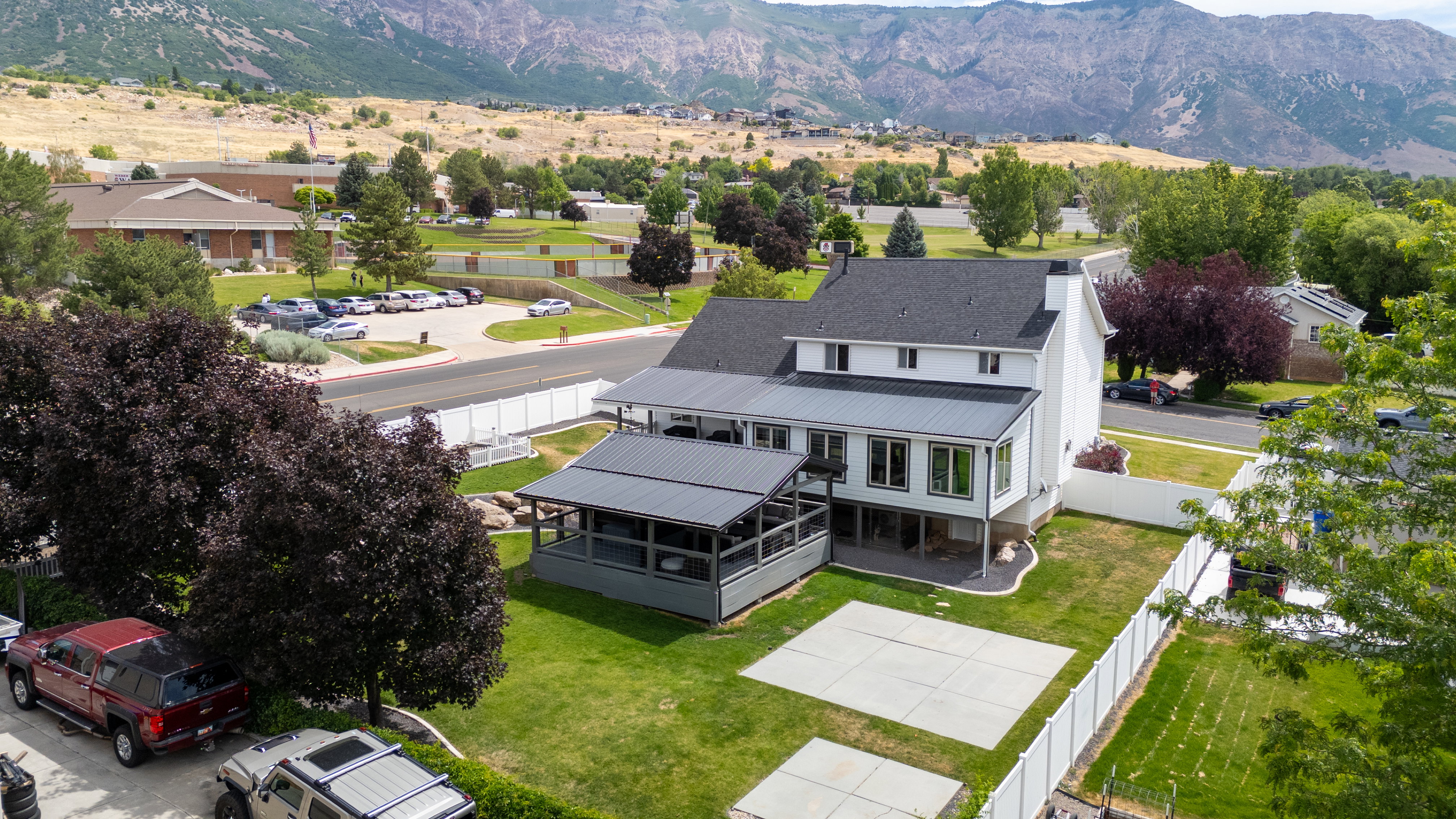 Aerial rear view exterior featuring white siding, a dark shingled roof, and a covered back patio with a dark metal roof