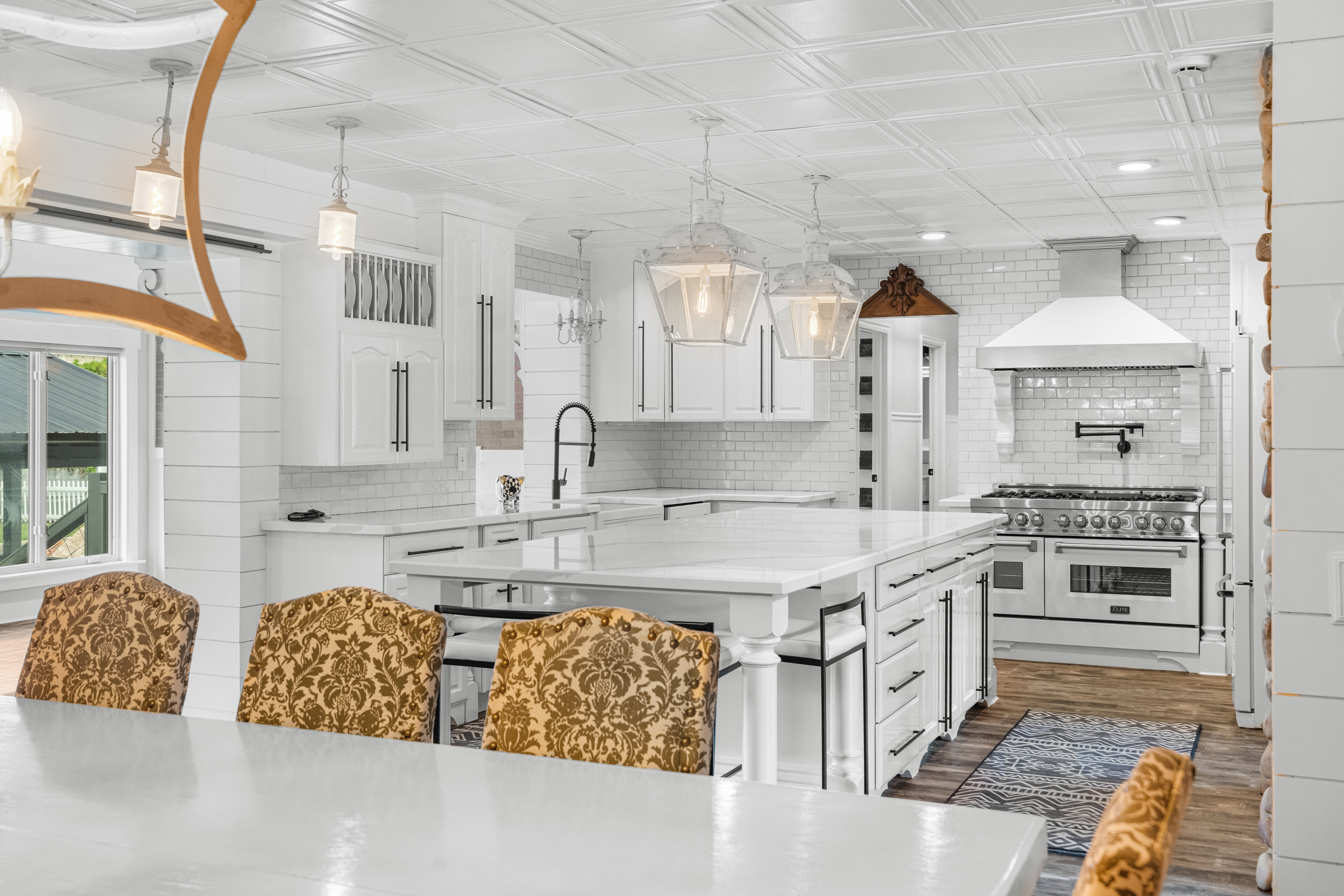 Expansive kitchen featuring an oversized island with seating, white shaker cabinetry, subway tile backsplash, and a large professional-style range with a matching vent hood